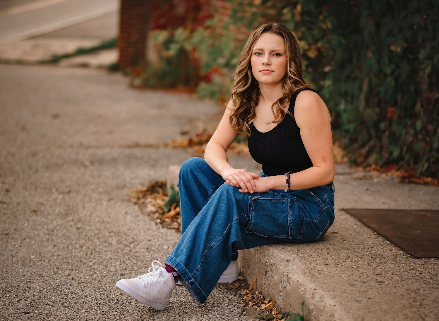 Someone in casual denim and a black tank top sits on a concrete curb.