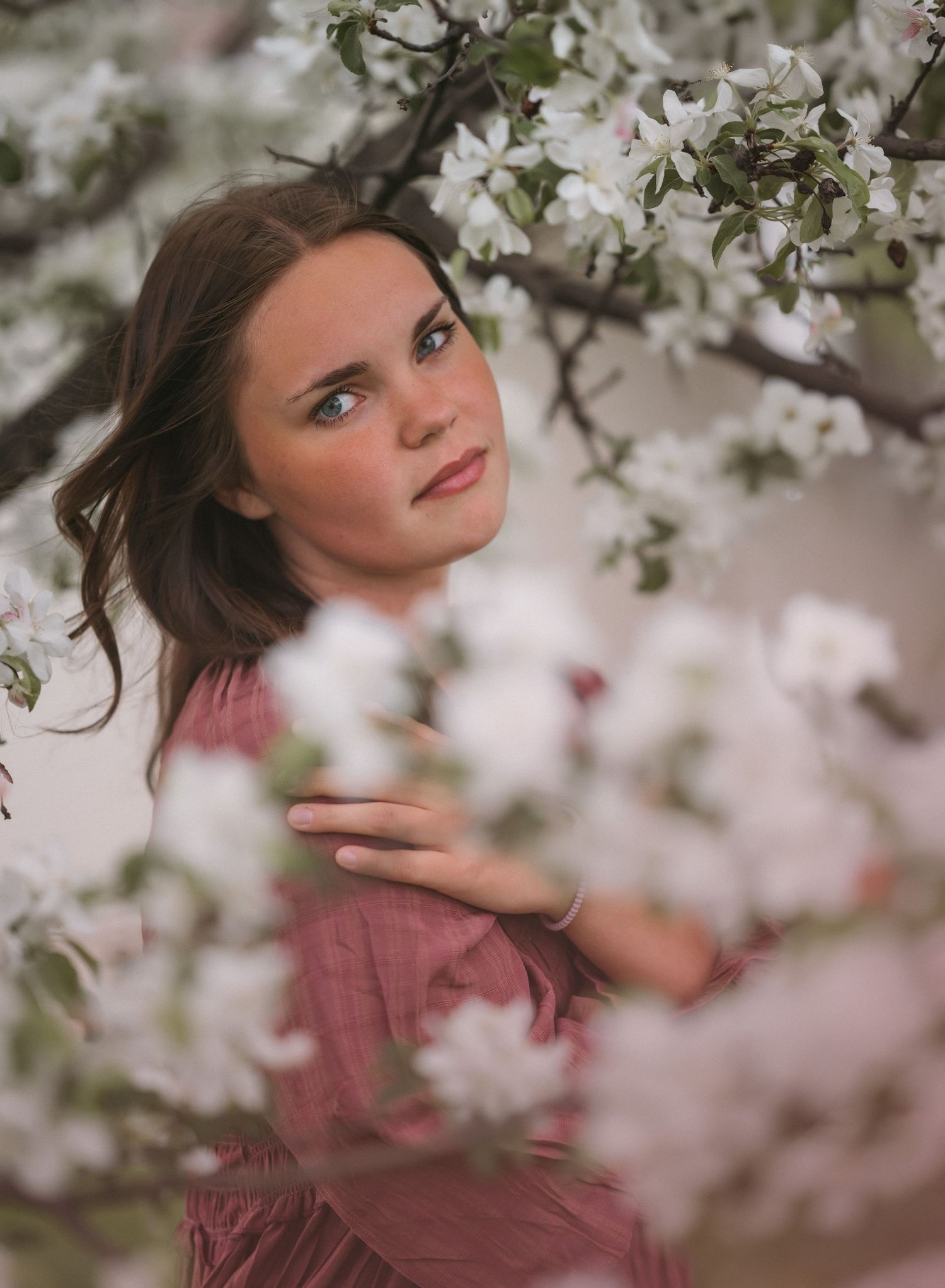 Ethereal spring portrait framed by delicate cherry blossoms in soft pink lighting.