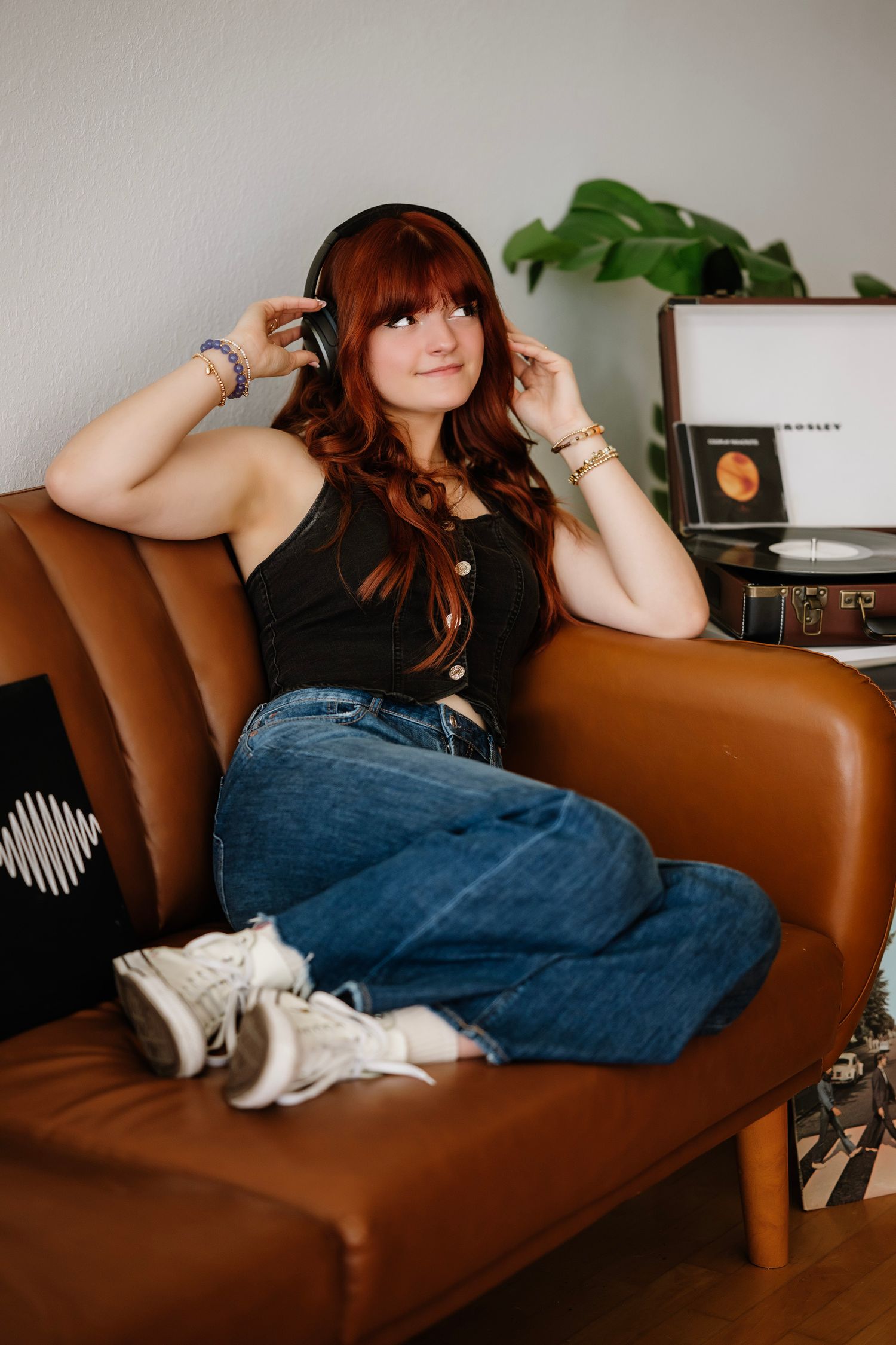 Person lounges on brown leather couch in denim jeans with white sneakers visible in a cozy home setting.