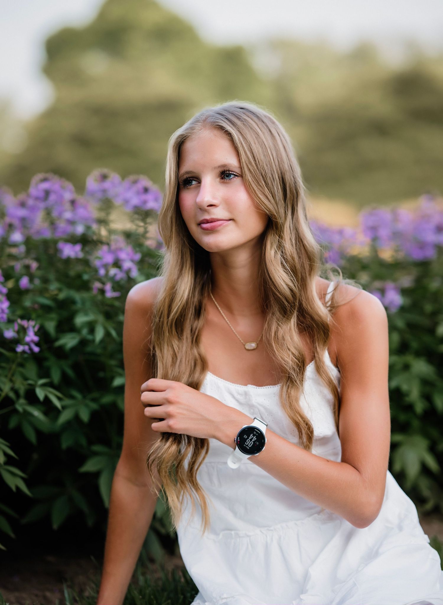 A person in a white dress poses in a field of purple wildflowers during a summer photo session.
