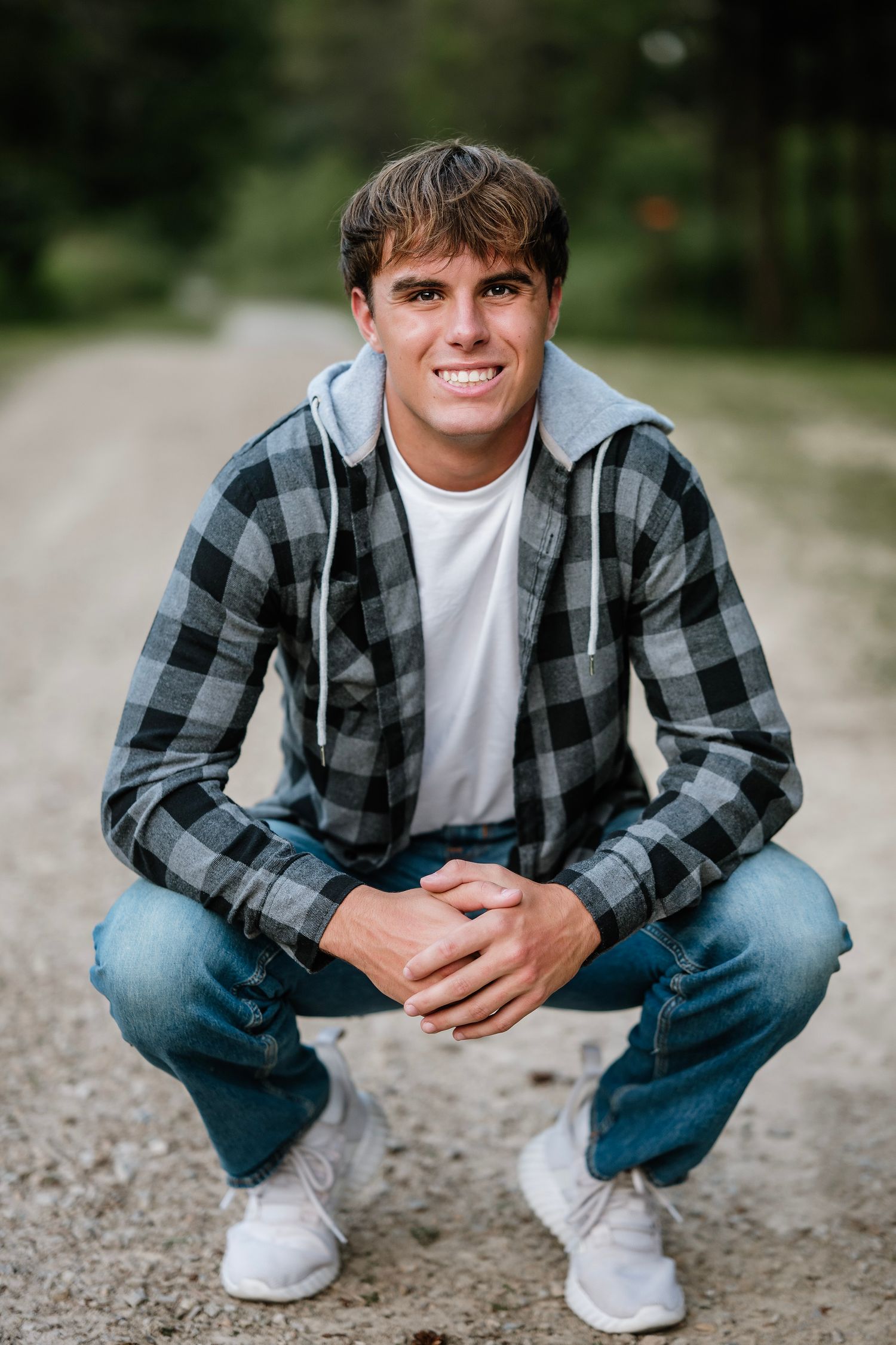 A person wearing a plaid flannel shirt and jeans crouches on a gravel path in an outdoor setting.
