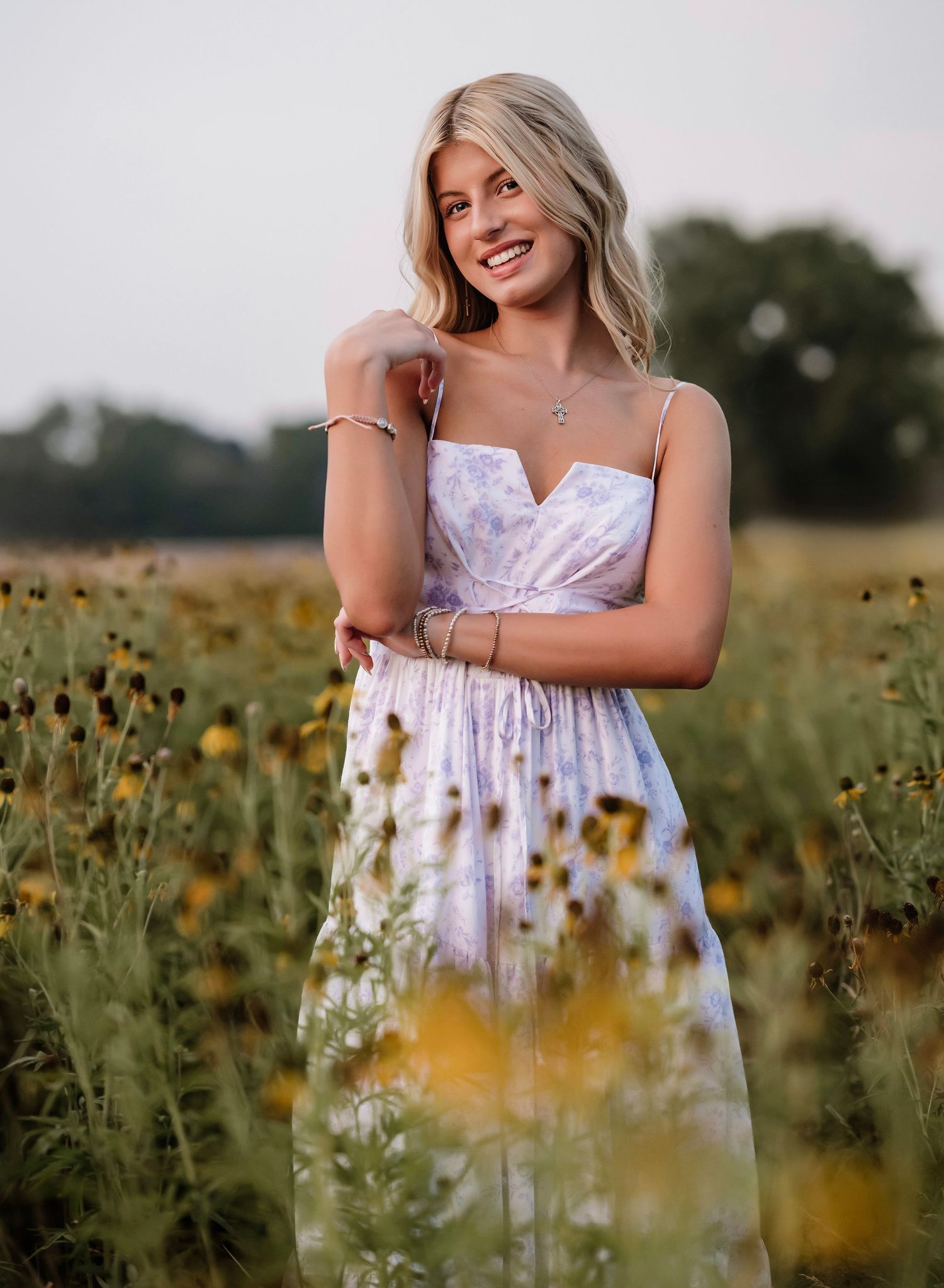 A figure in a white sundress stands among vibrant wildflowers in a golden meadow during sunset.