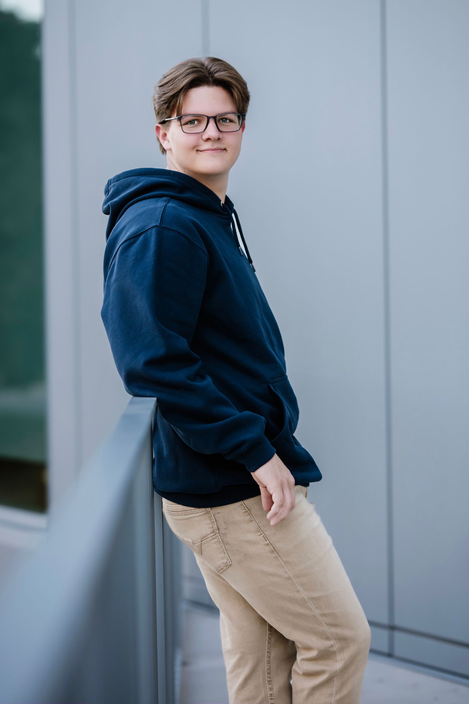 Four similar photos show someone in a navy hoodie and khaki pants posing against a light gray wall.
