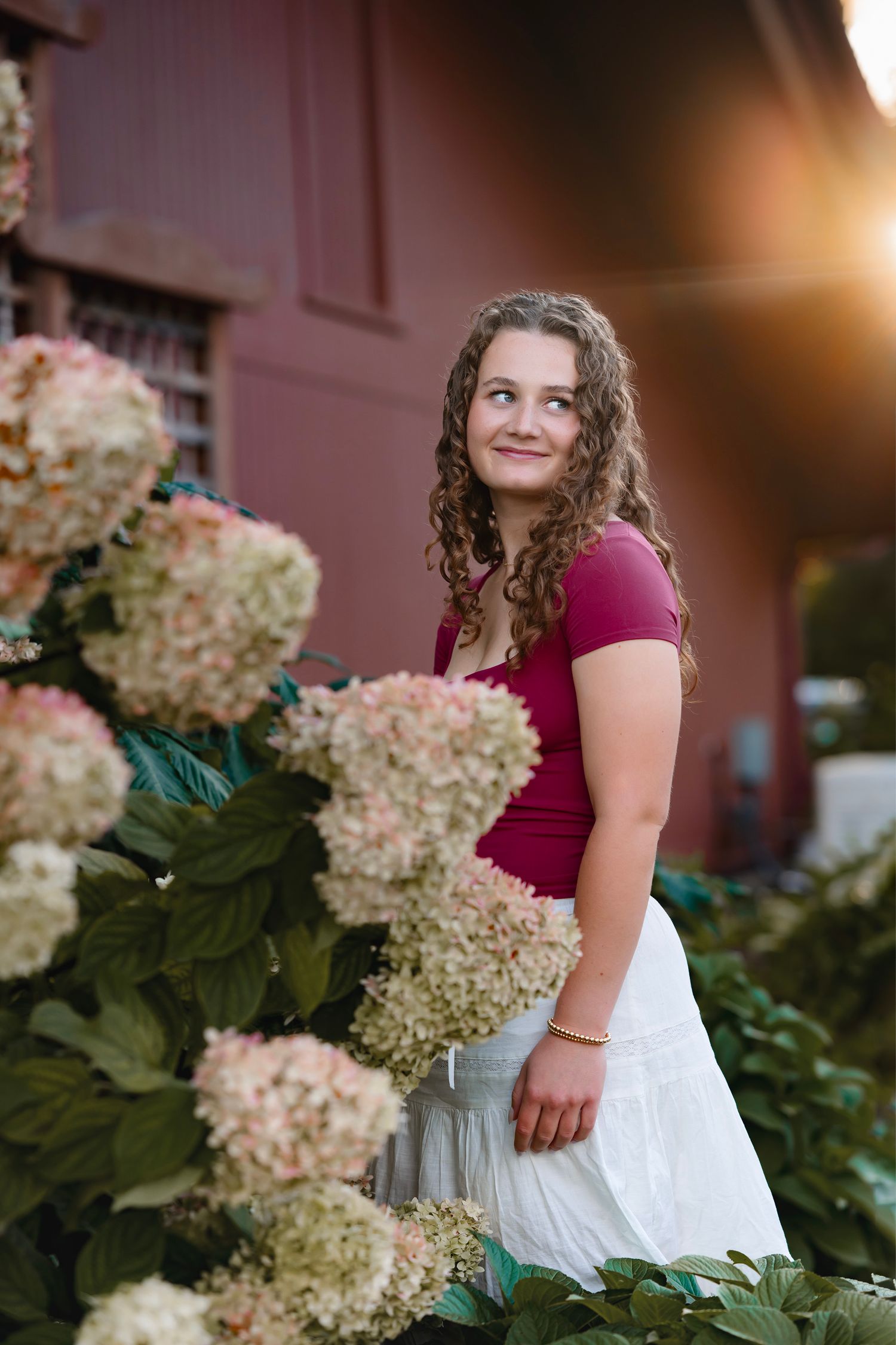 A figure in a white dress sits among blooming hydrangea flowers at sunset creating a dreamy outdoor portrait.