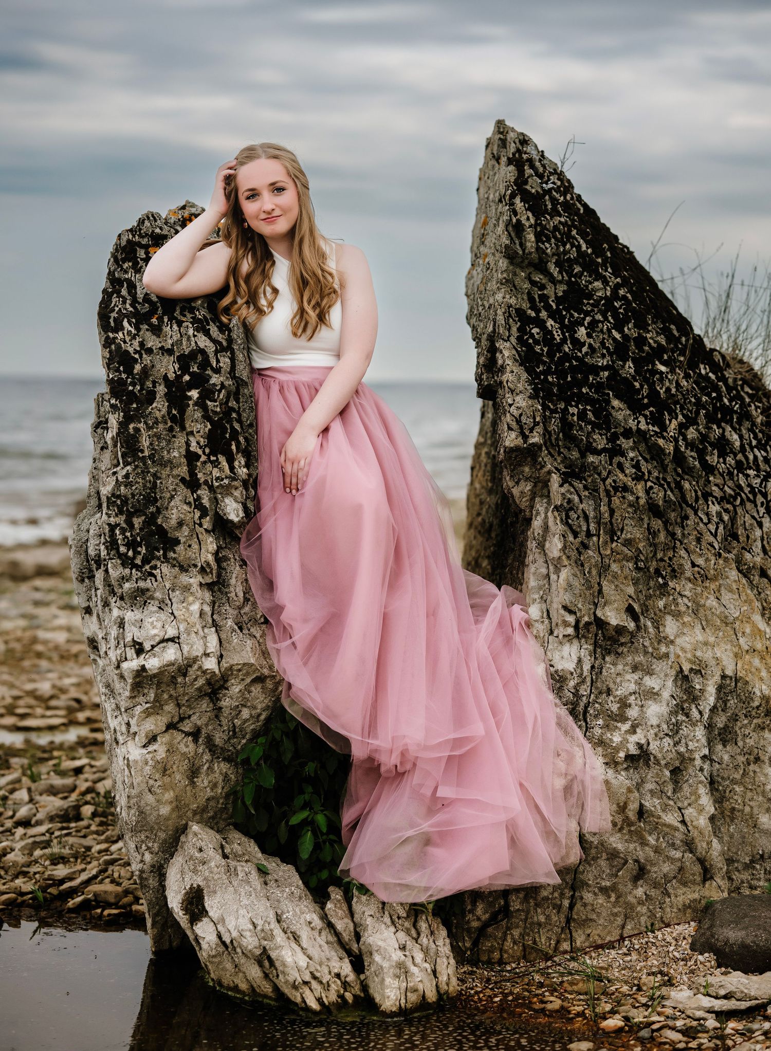A dreamy senior portrait session featuring a pink tulle dress against weathered rocks on a moody beach.