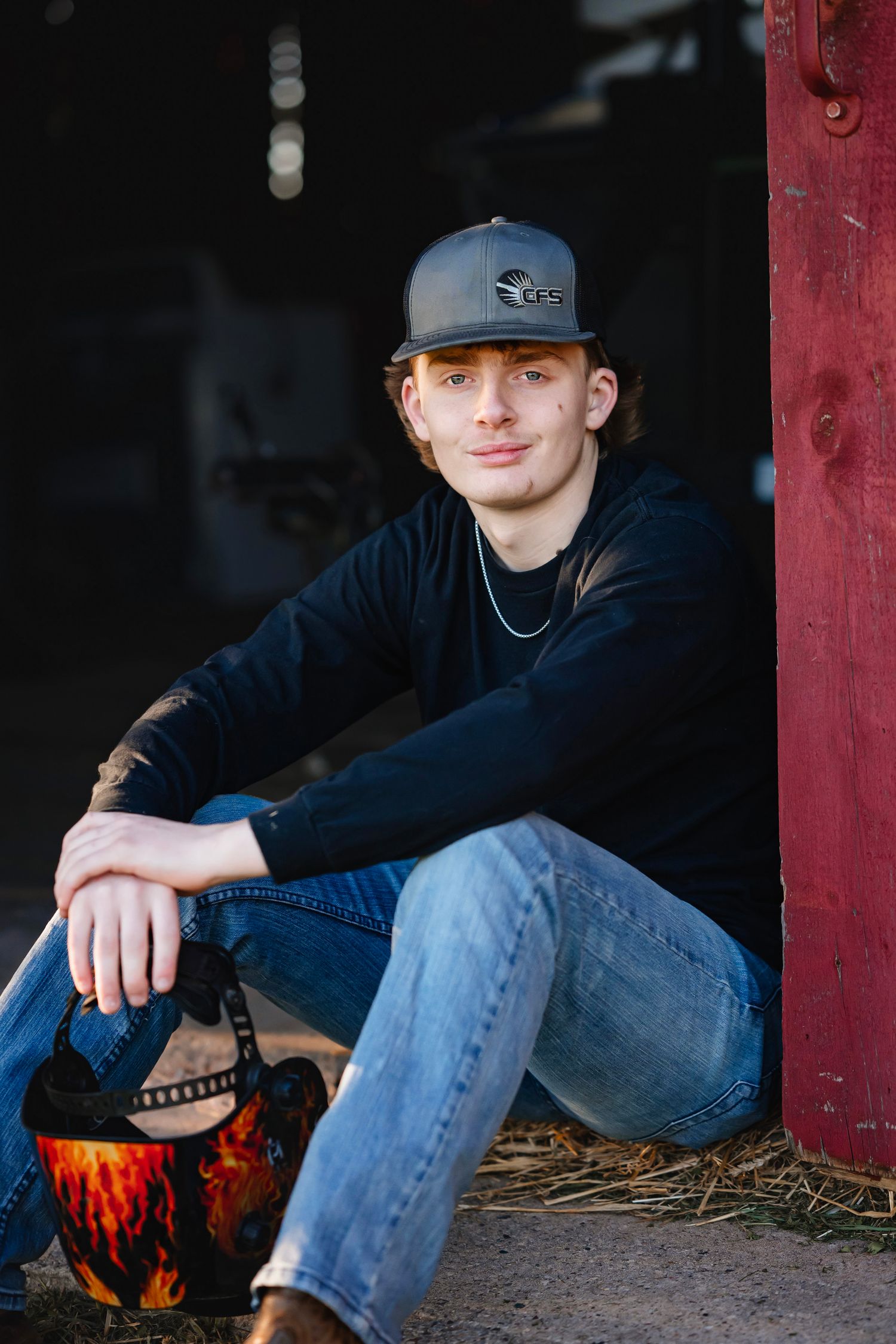 A casual portrait in a barn doorway showing someone wearing a baseball cap, navy shirt and jeans in natural light.