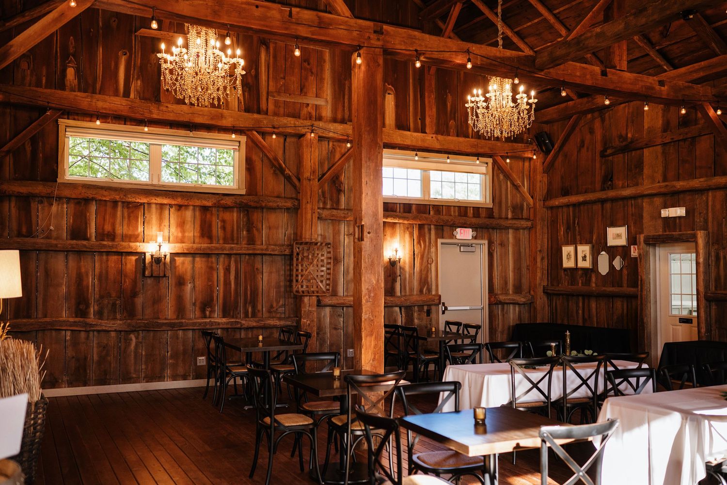 Rustic barn wedding venue with chandeliers, wooden beams, and elegant table settings on hardwood floors.