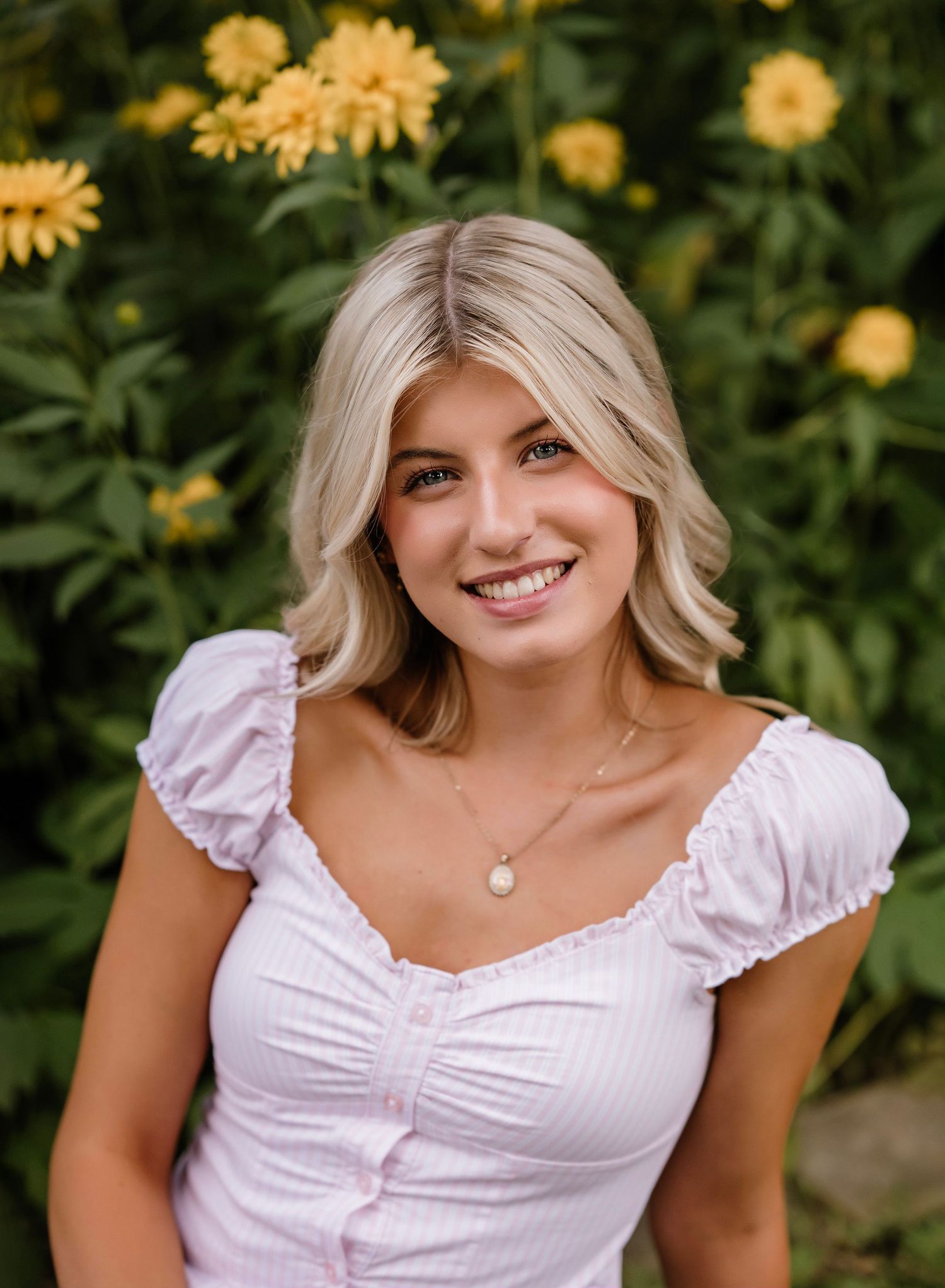 Woman in white summer dress poses in garden with yellow flowers in background.