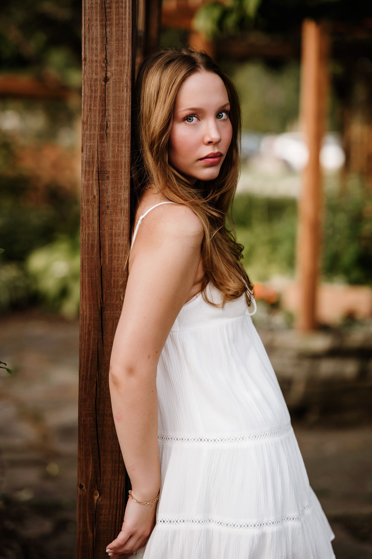Artistic senior portrait against a wooden post wearing a flowing white tiered dress.