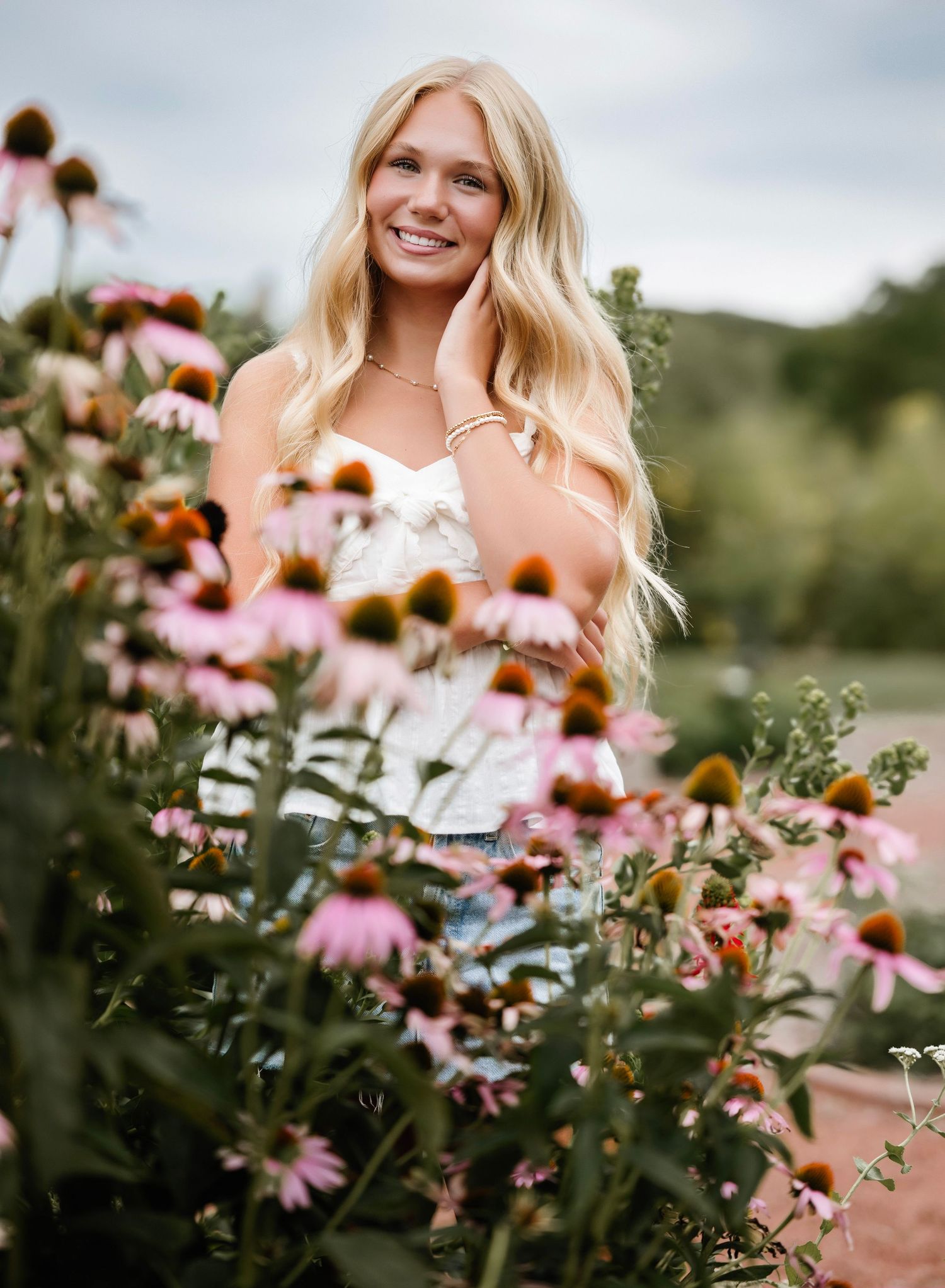 A woman in a white dress stands among blooming pink coneflowers in a summer garden setting.