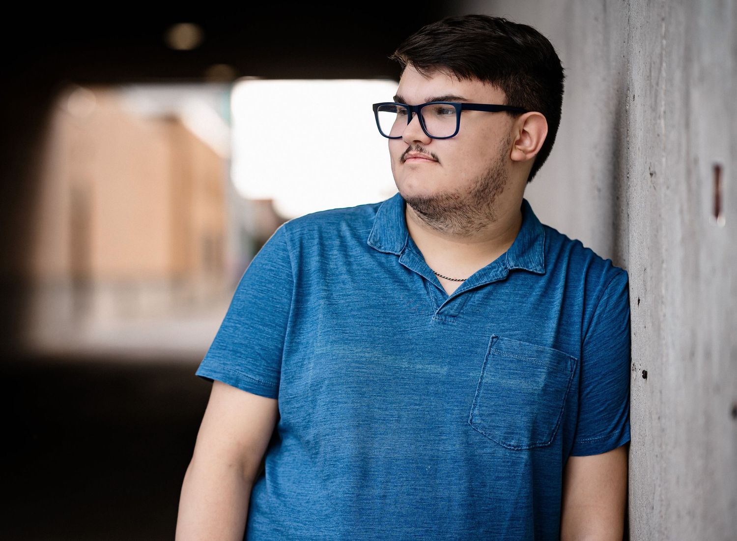 A casual senior portrait in blue t-shirt against an urban concrete backdrop.