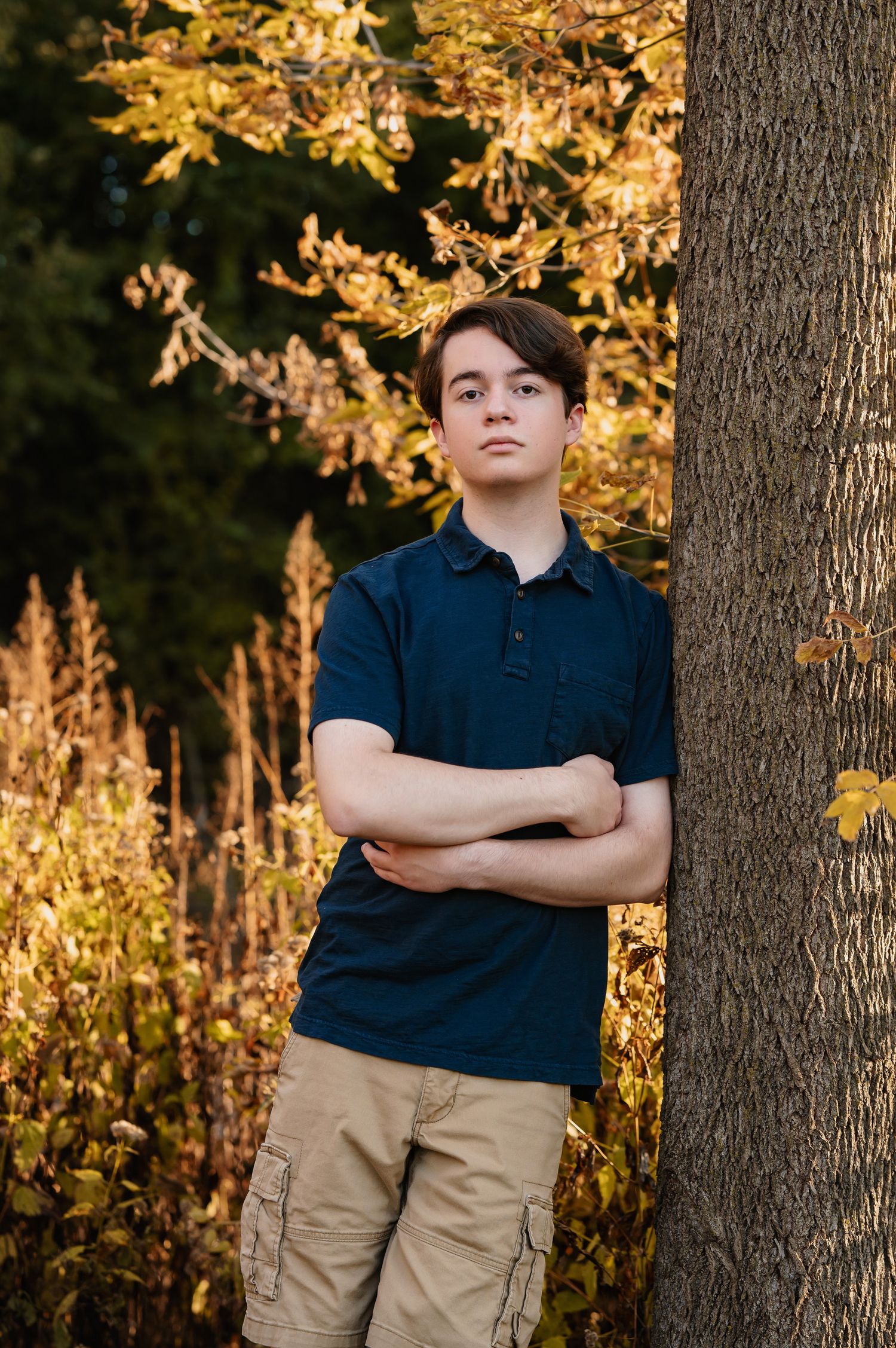 A navy polo and khaki cargo pants compose a casual look against golden autumn foliage.