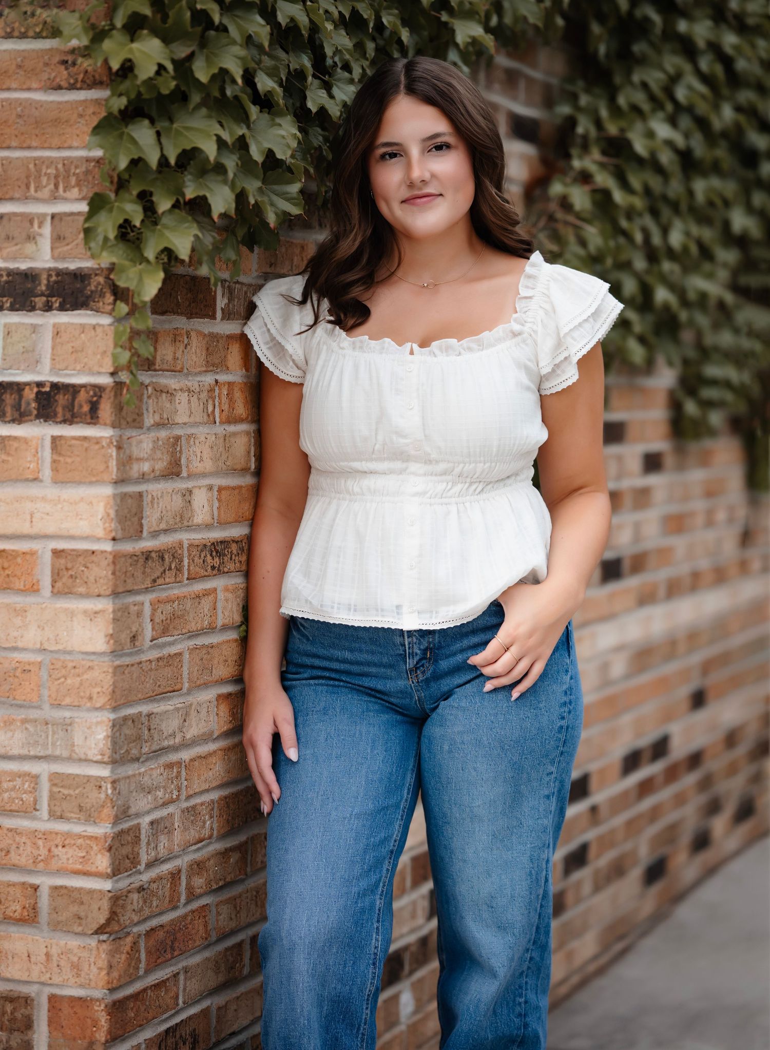 Casual outdoor fashion photography featuring a white peasant top and blue jeans against a brick wall with ivy backdrop.