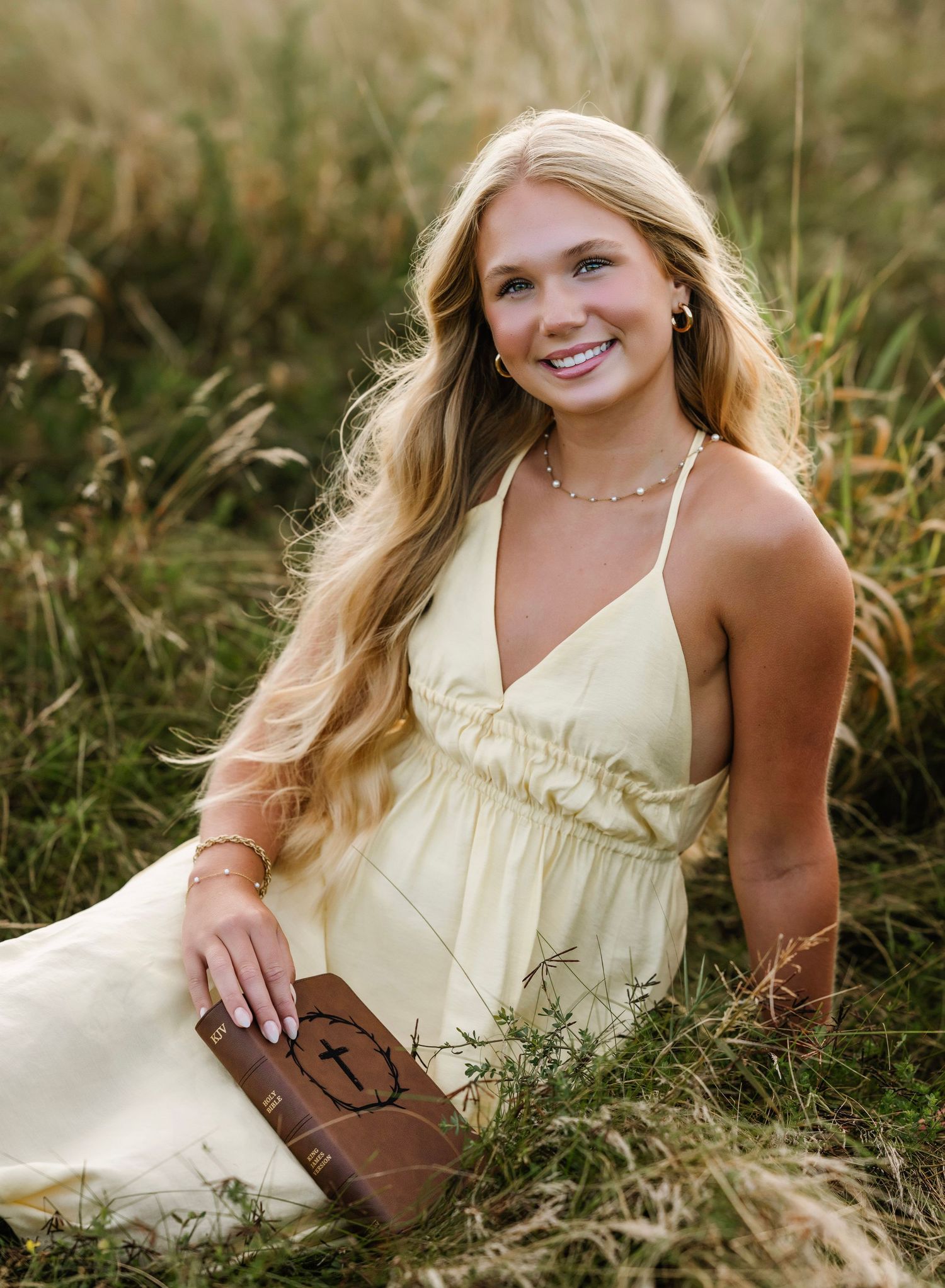 A person in a pale yellow sundress poses gracefully in tall grass during a summer photoshoot.
