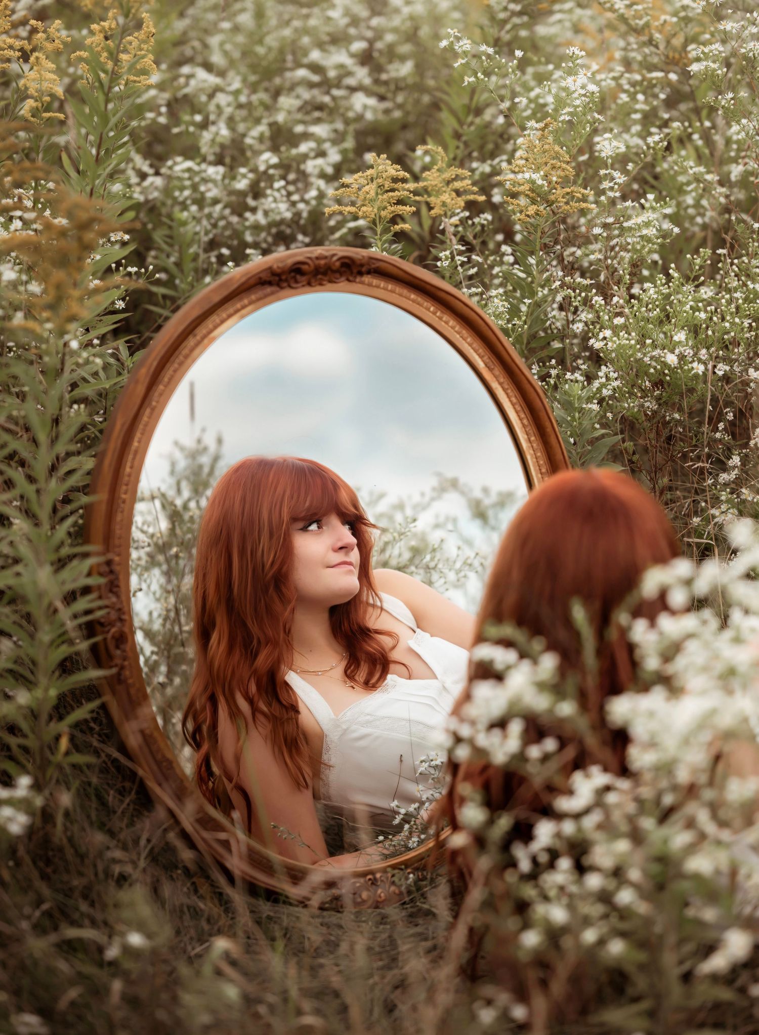 A round mirror reflects a dreamy scene in a field of white wildflowers on a sunny summer day.