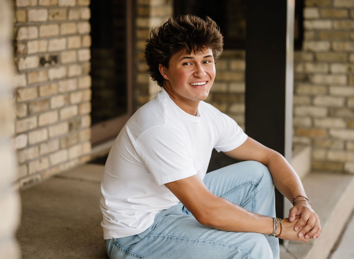 A person in a white t-shirt and jeans sits casually on a brick ledge with natural lighting.