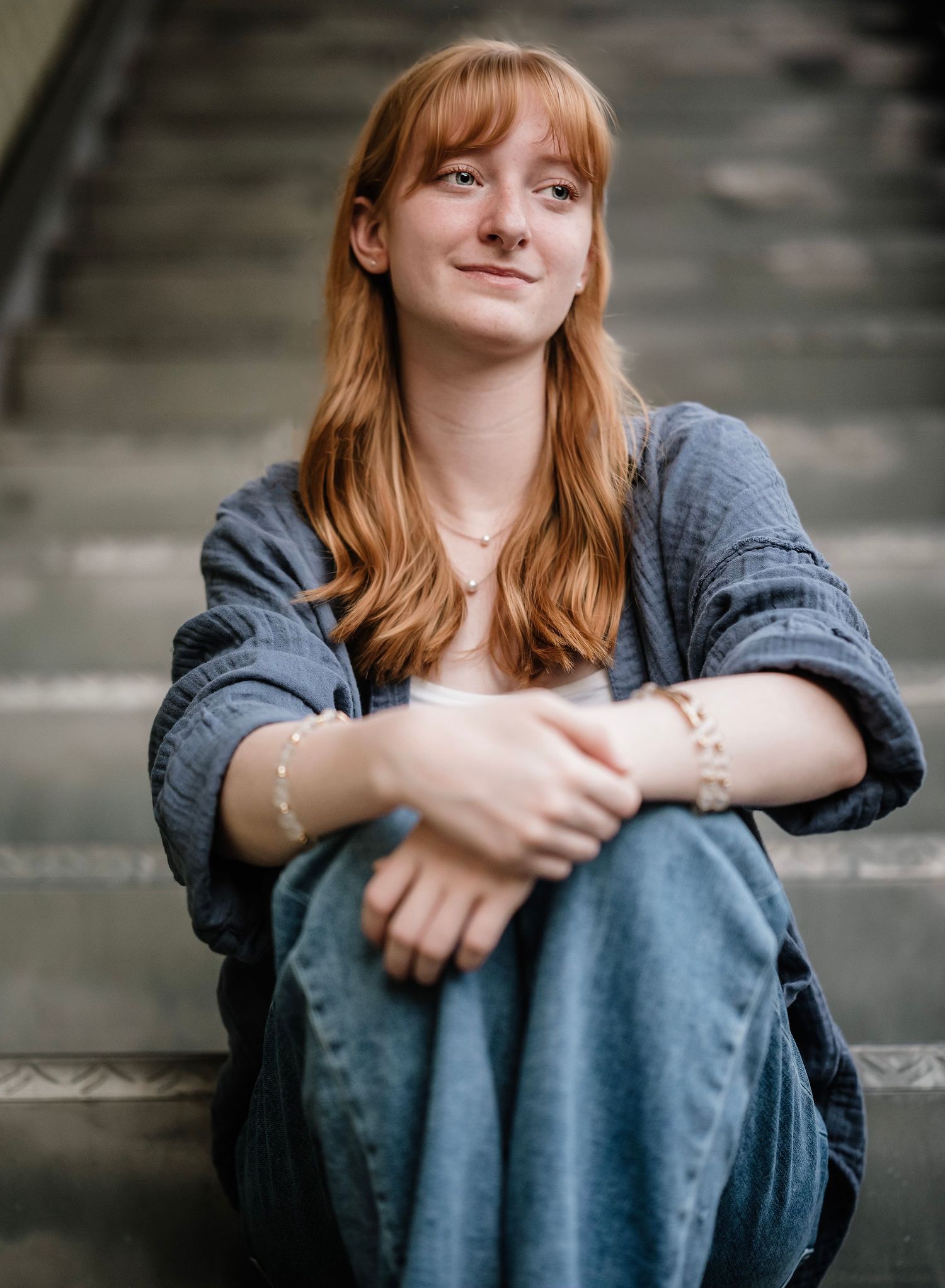 Person wearing denim jacket sits outdoors in contemplative poses against blurred background.