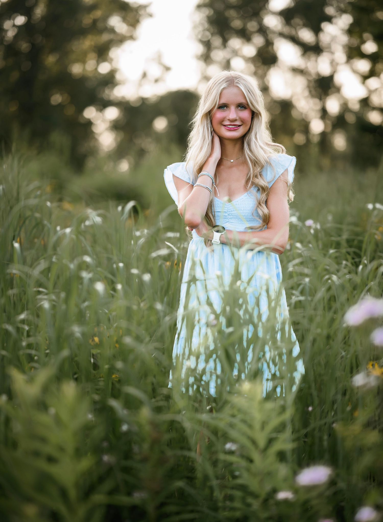 A person in a light blue dress stands among tall wildflowers in a dreamy summer meadow at golden hour.