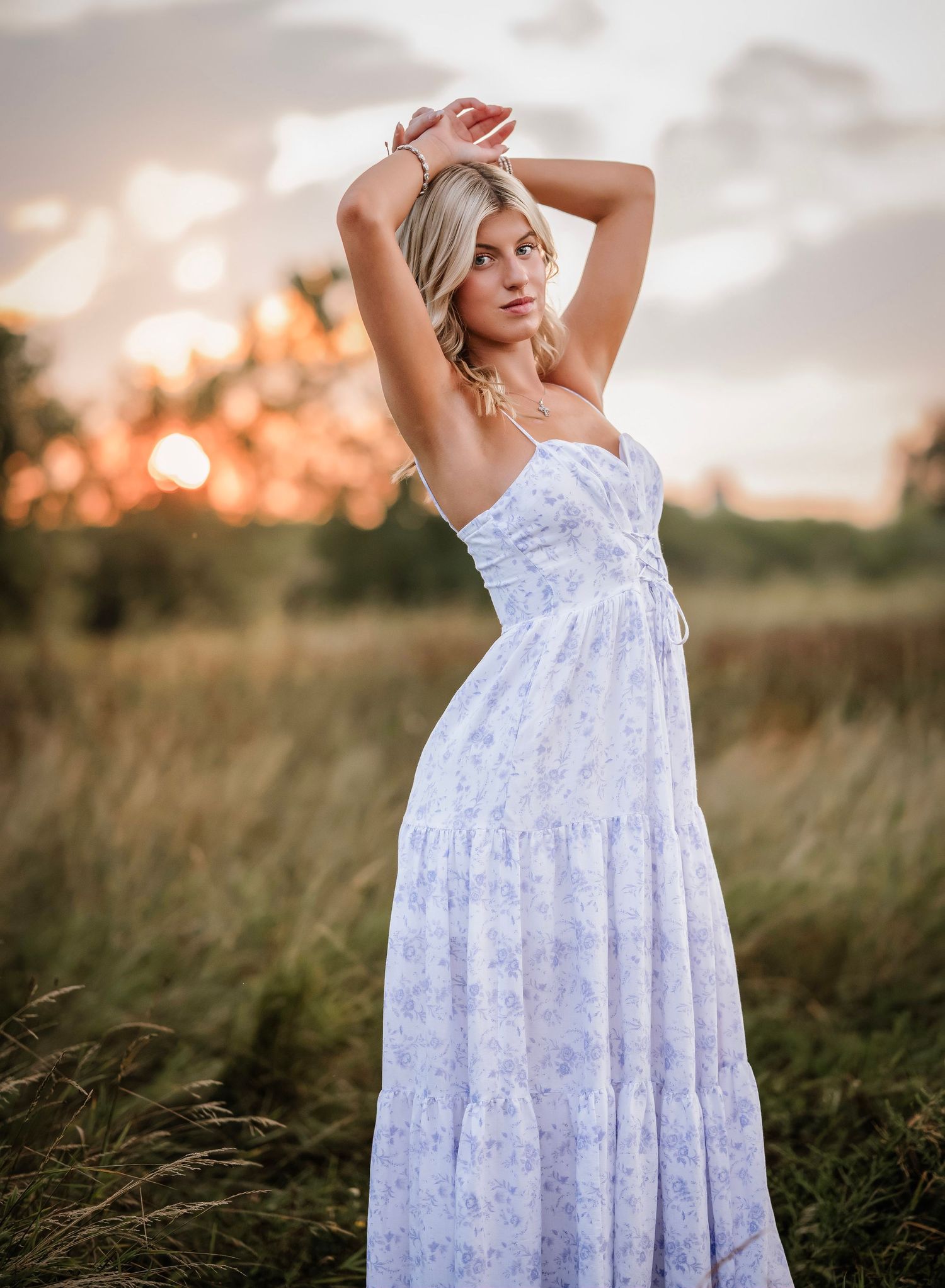 A white floral sundress flows elegantly in a golden field during sunset, creating a dreamy summer portrait.