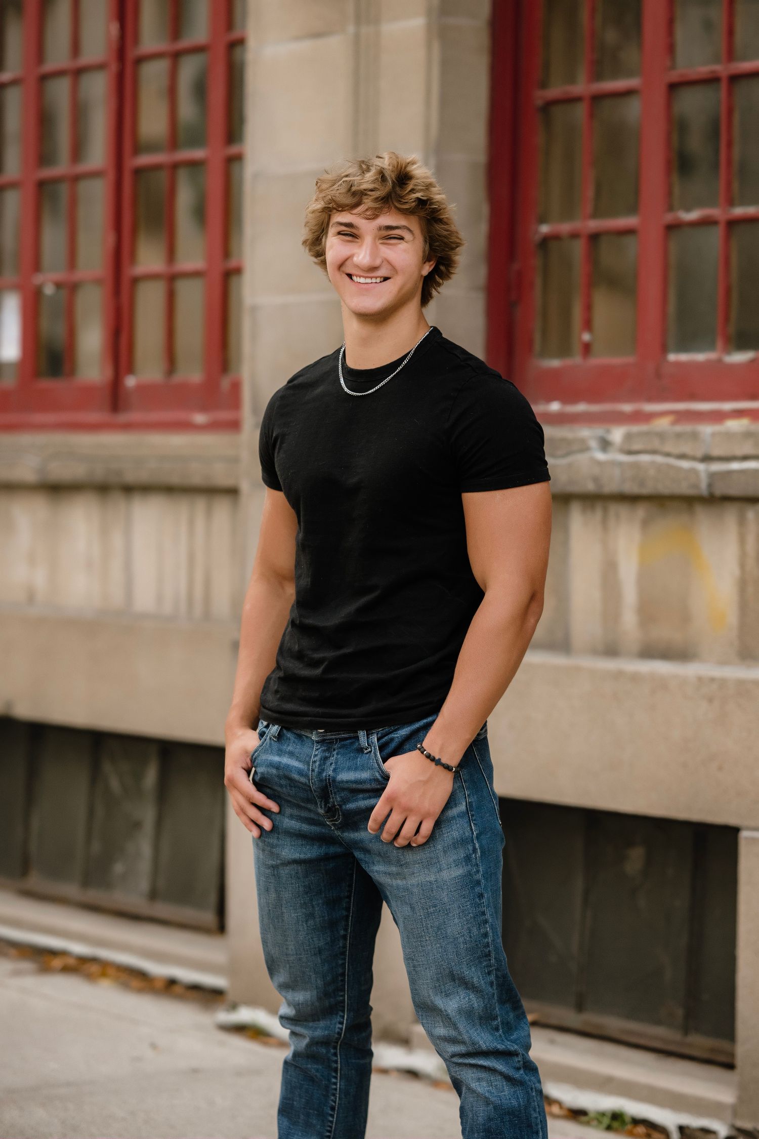 A casual portrait series showing someone wearing a black t-shirt and jeans against a brick building with red windows.