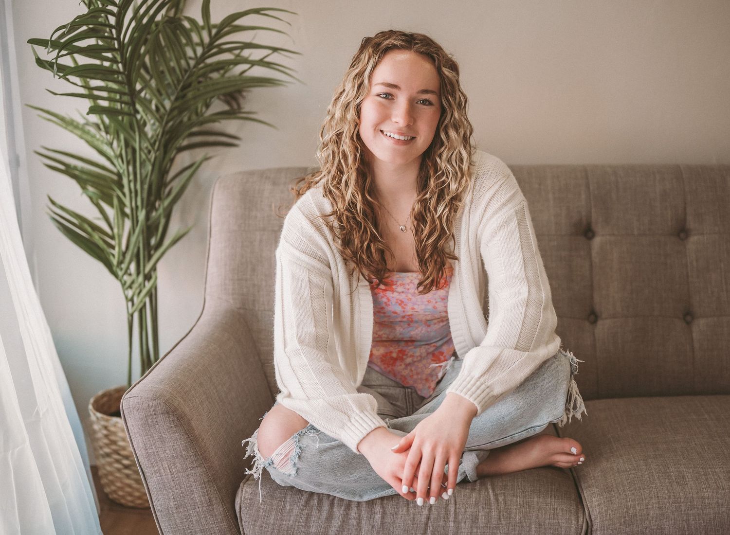 A relaxed indoor portrait on a gray couch with a tropical plant in the background.