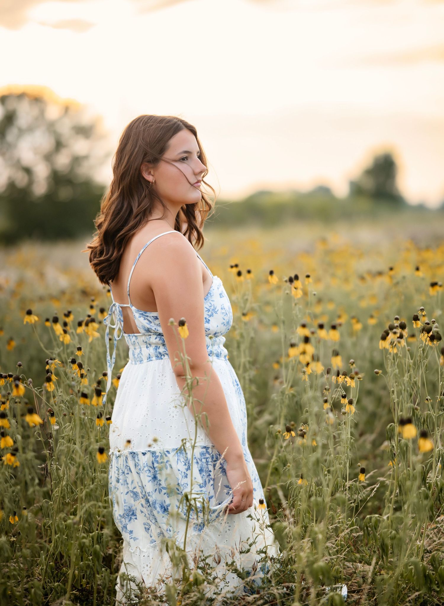 A dreamy sunset photoshoot in a field of yellow wildflowers with soft golden light filtering through the summer evening.