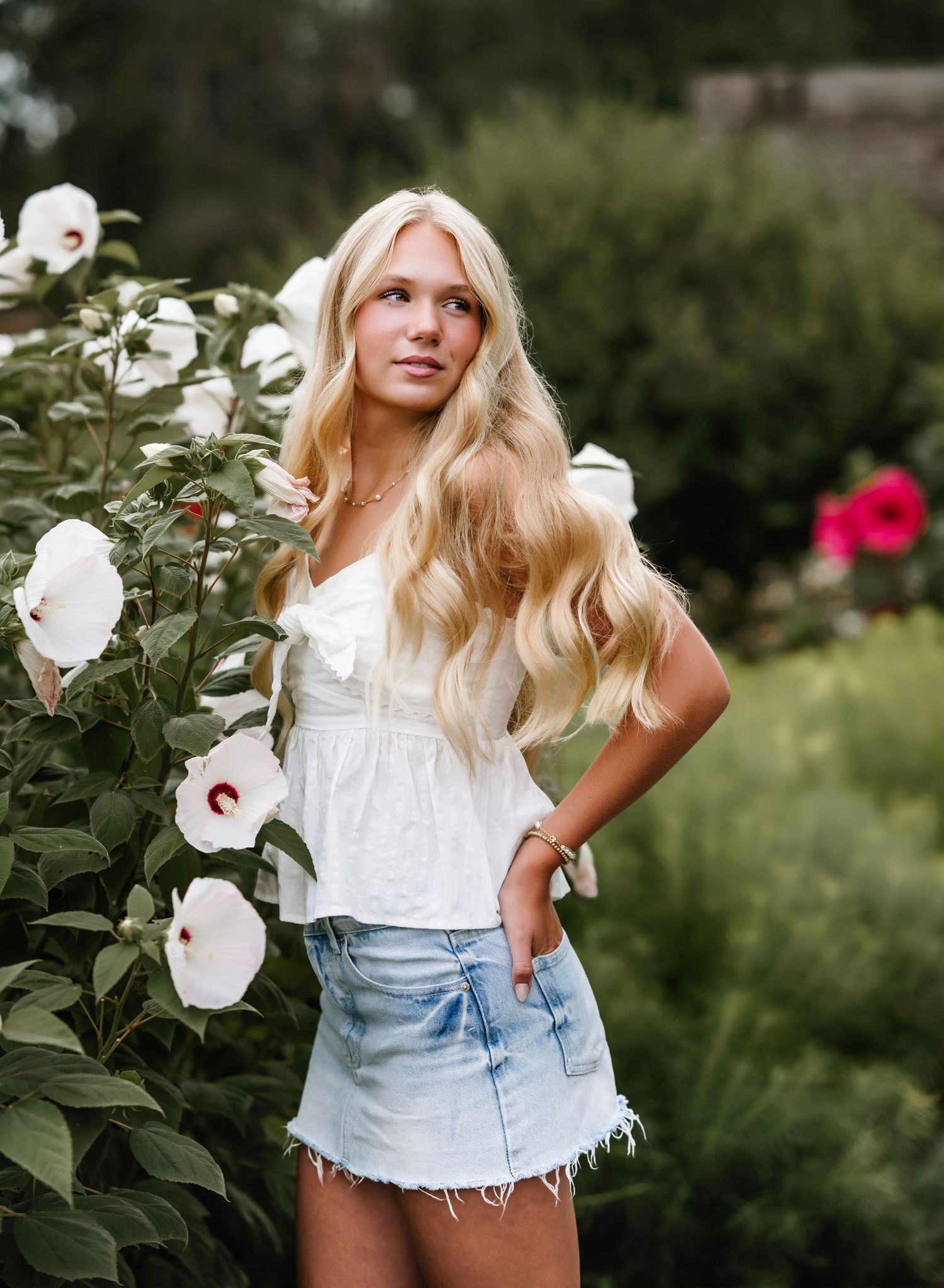 A white lace top and denim shorts outfit styled in a garden with blooming white hibiscus flowers.