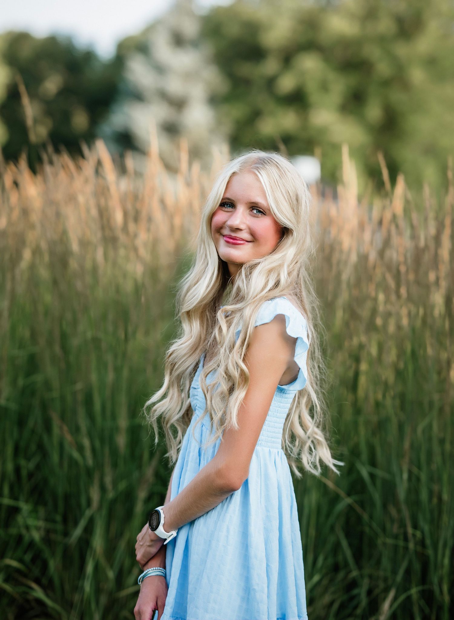 A light blue summer dress is worn in a field of tall grass during golden hour.