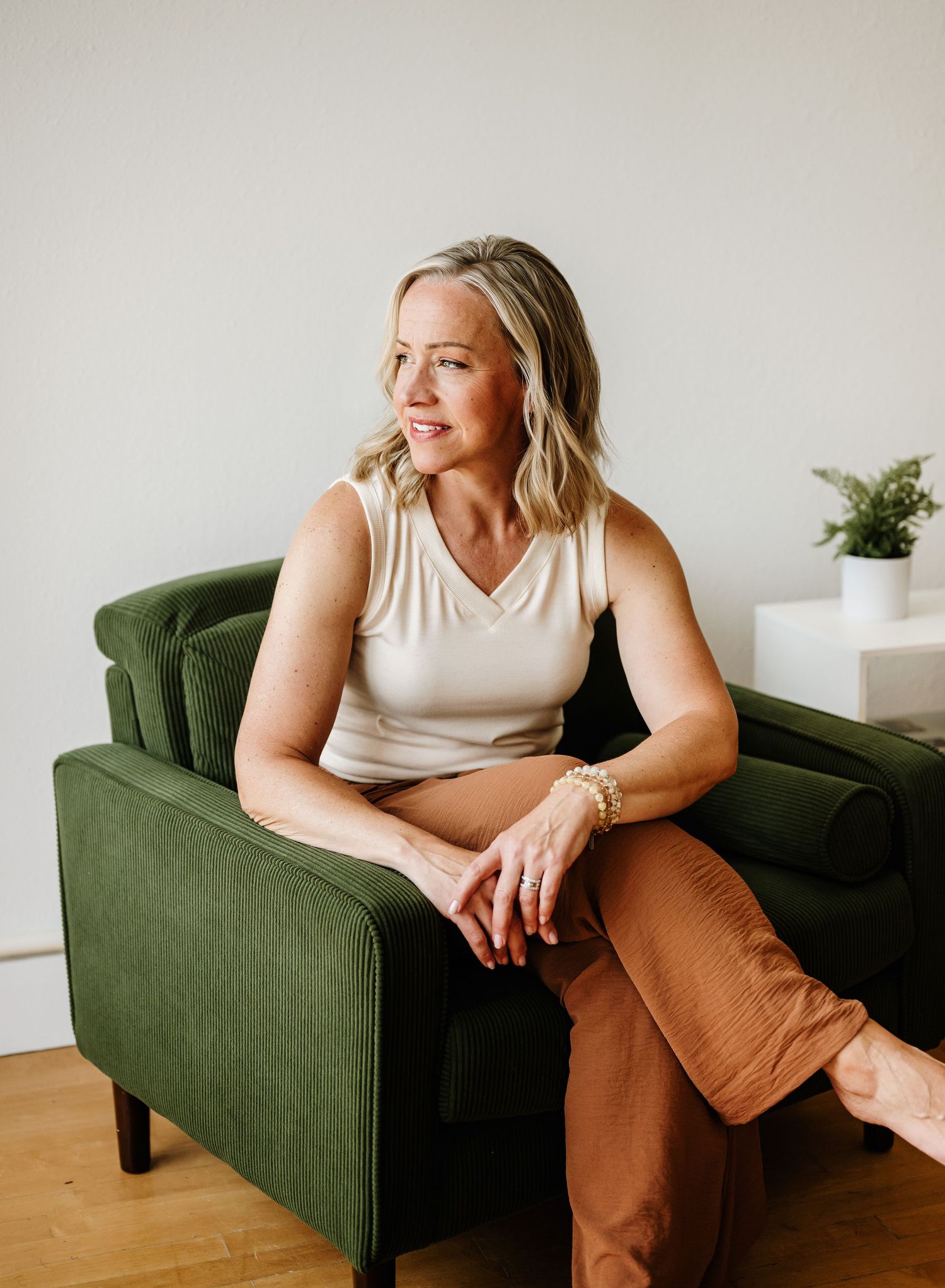 A person in casual attire sits relaxed on an olive green armchair against a white wall in a minimalist setting.