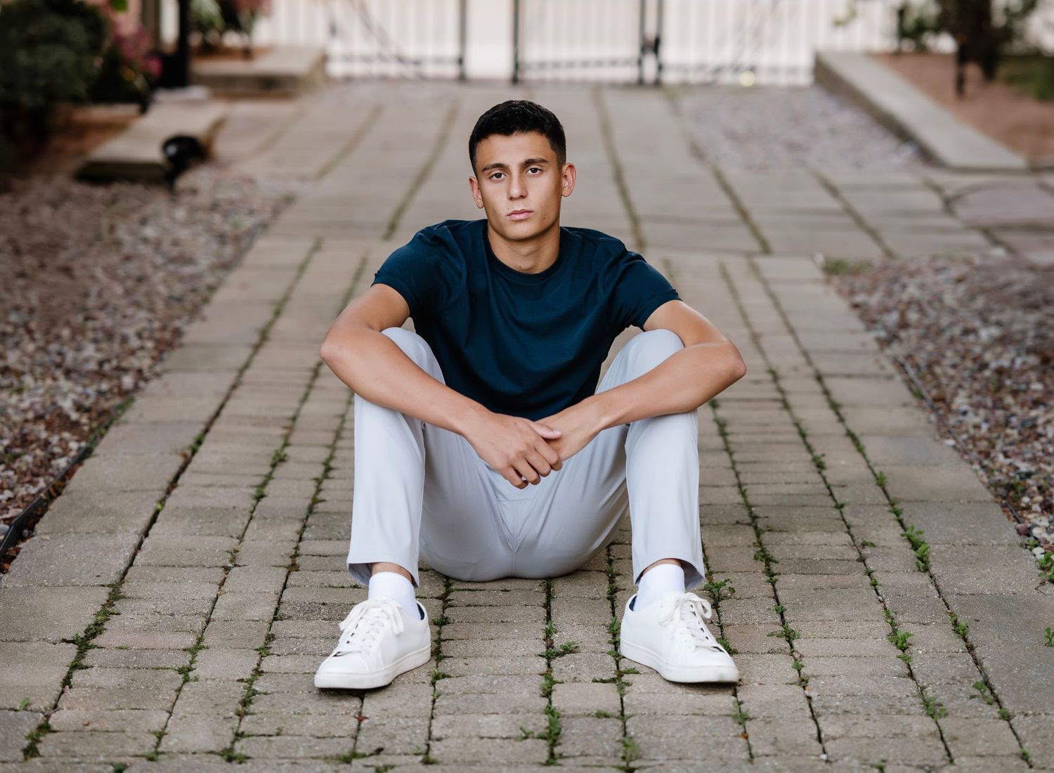 A person in a navy t-shirt and white pants sits on a stone pathway wearing white sneakers.
