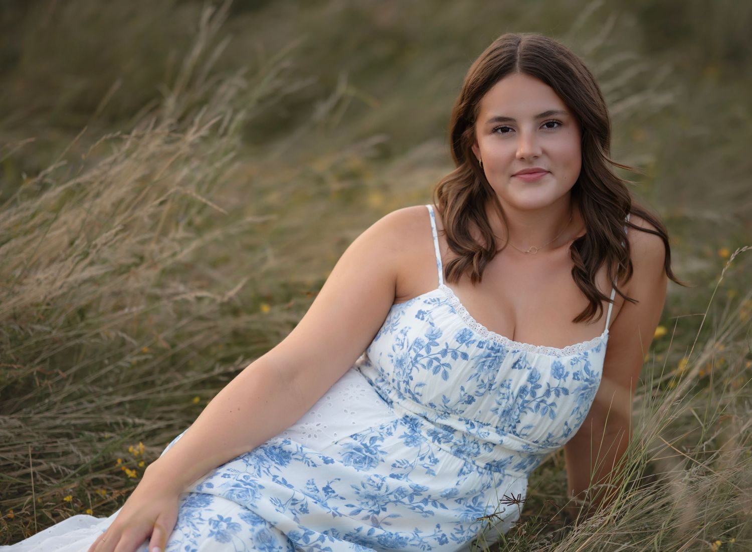 A person in a blue and white floral dress poses gracefully in a field of tall grass during golden hour.