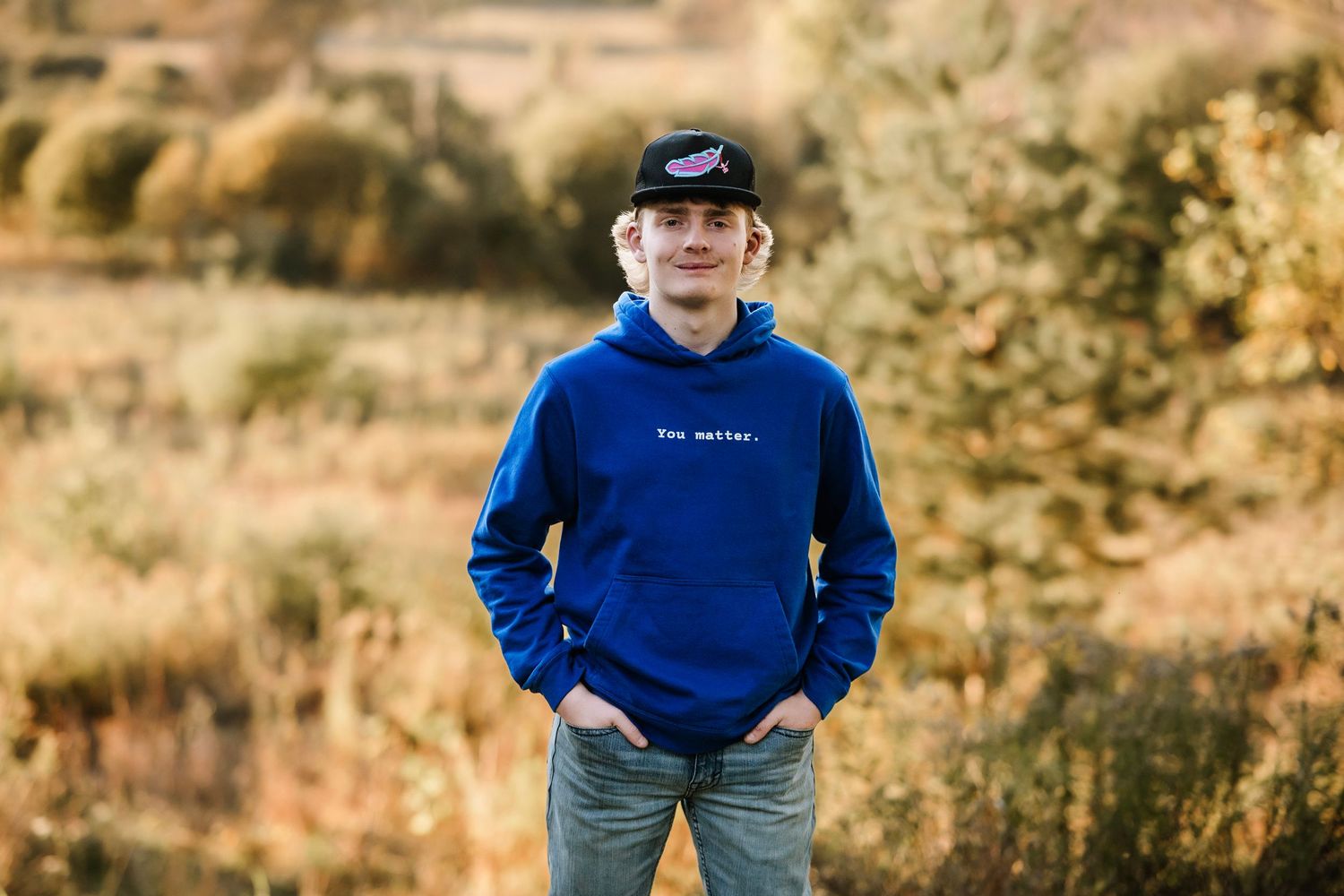 A person in a blue sweatshirt stands in a golden field during autumn sunset with warm lighting.