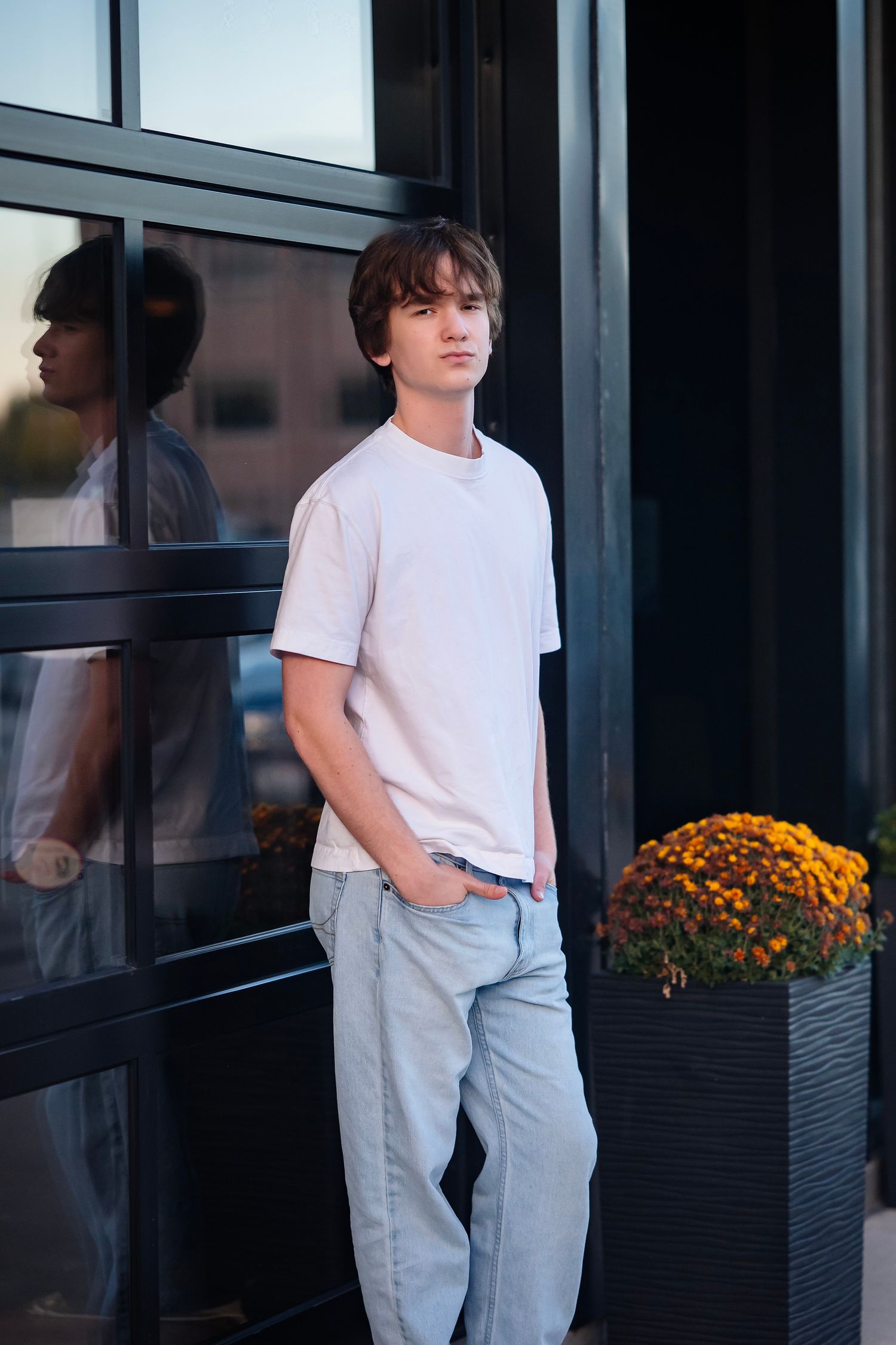 A person in a white t-shirt and light pants stands near black planters with orange flowers outdoors.