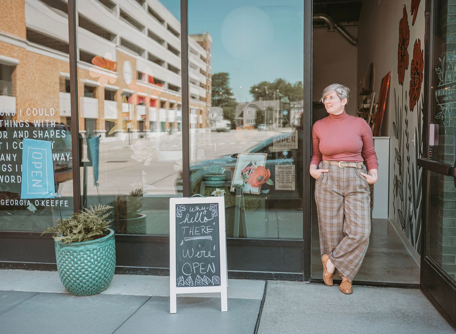 A retro-styled storefront with a turquoise planter and sidewalk chalkboard sign outside a small business entrance.