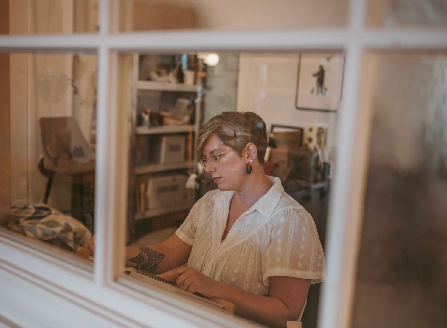 A person works at a wooden desk in a cozy home office with warm lighting and window views.