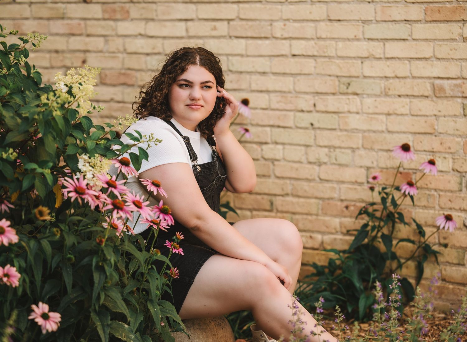 A floral garden portrait with pink flowers and a brick wall backdrop.