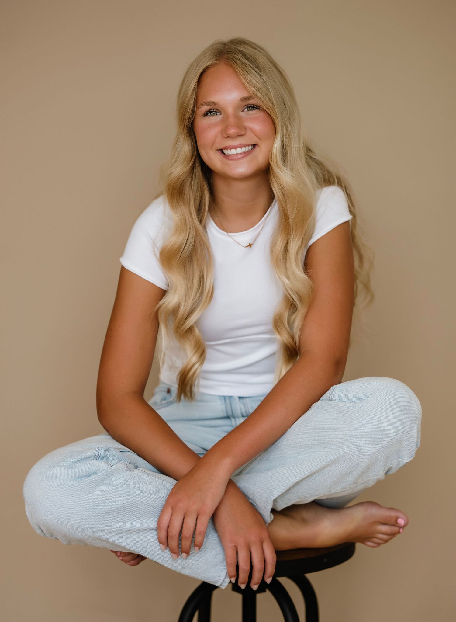A person wearing a white t-shirt and light blue pants poses casually in a series of studio portraits against a beige backdrop.