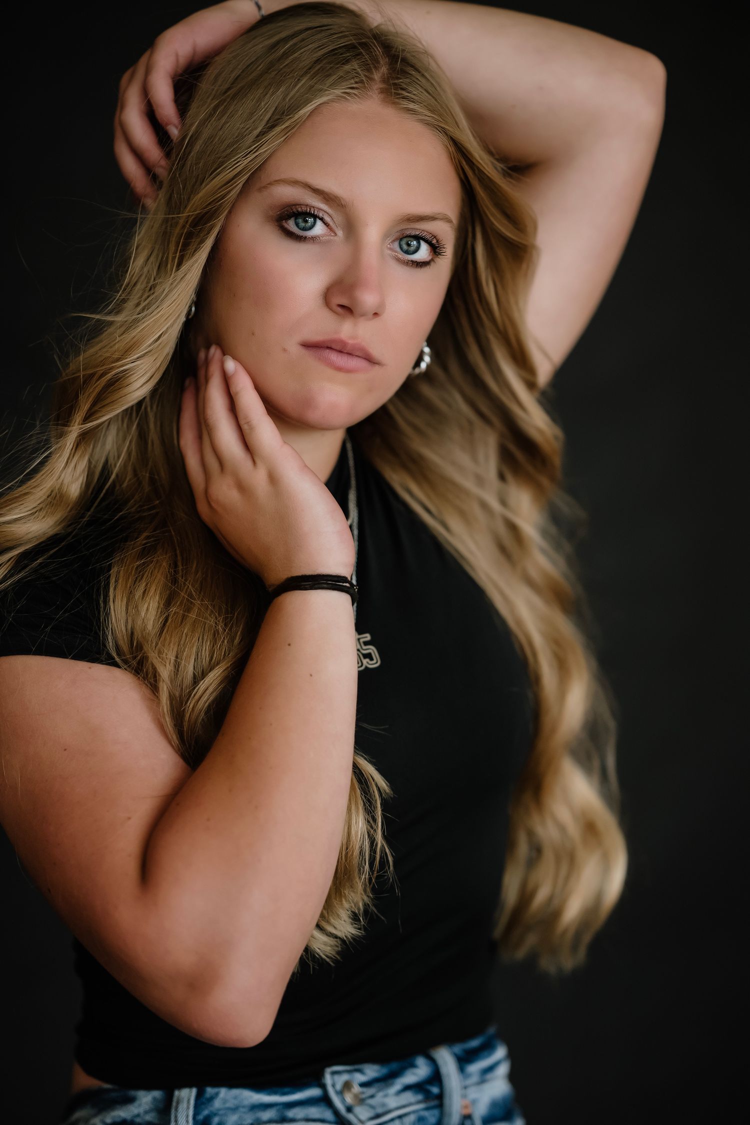 Portrait against dark background shows long wavy blonde hair and casual styling with black top and denim.