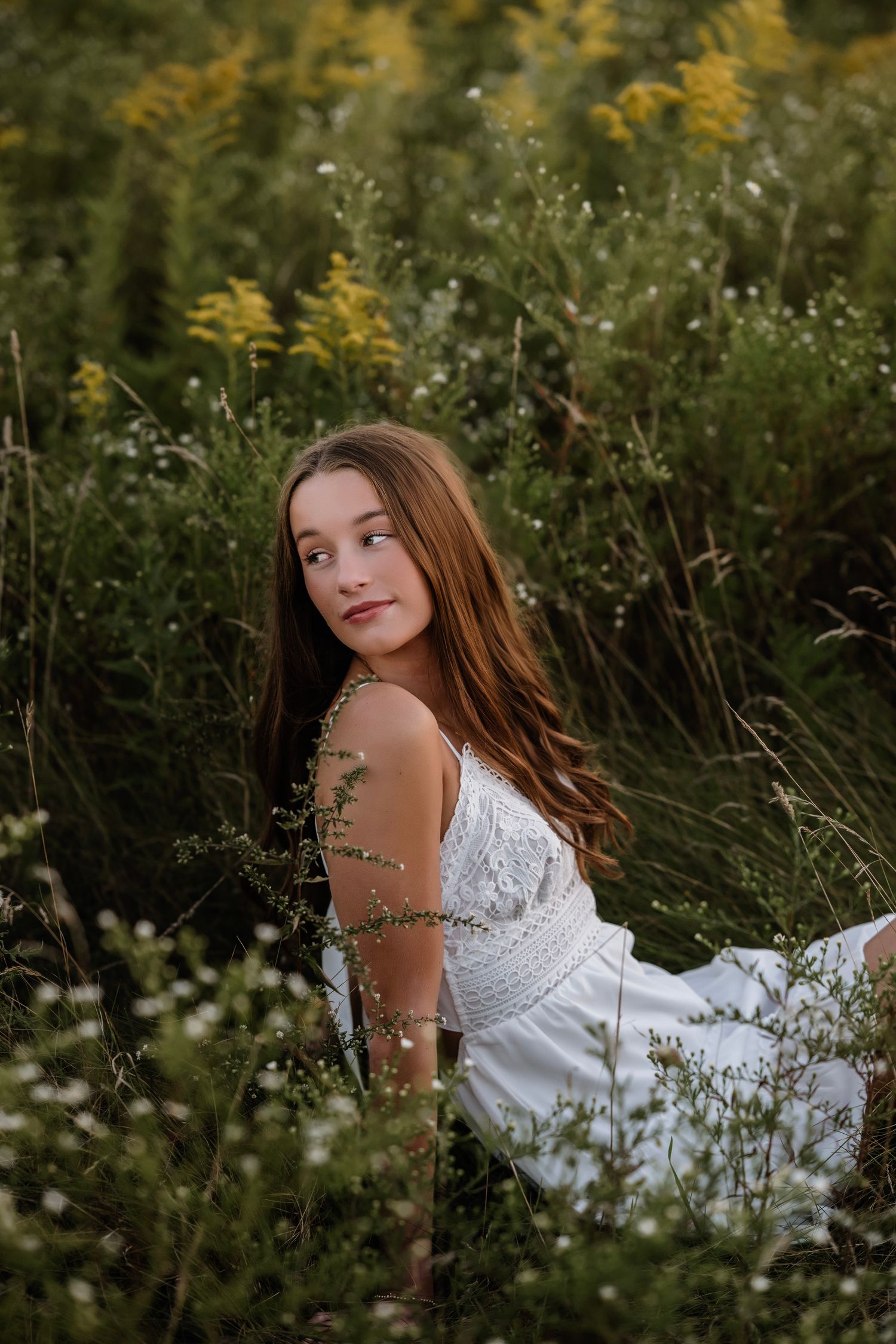 A dreamy outdoor portrait in a wildflower meadow with golden flowers and tall grass at sunset.