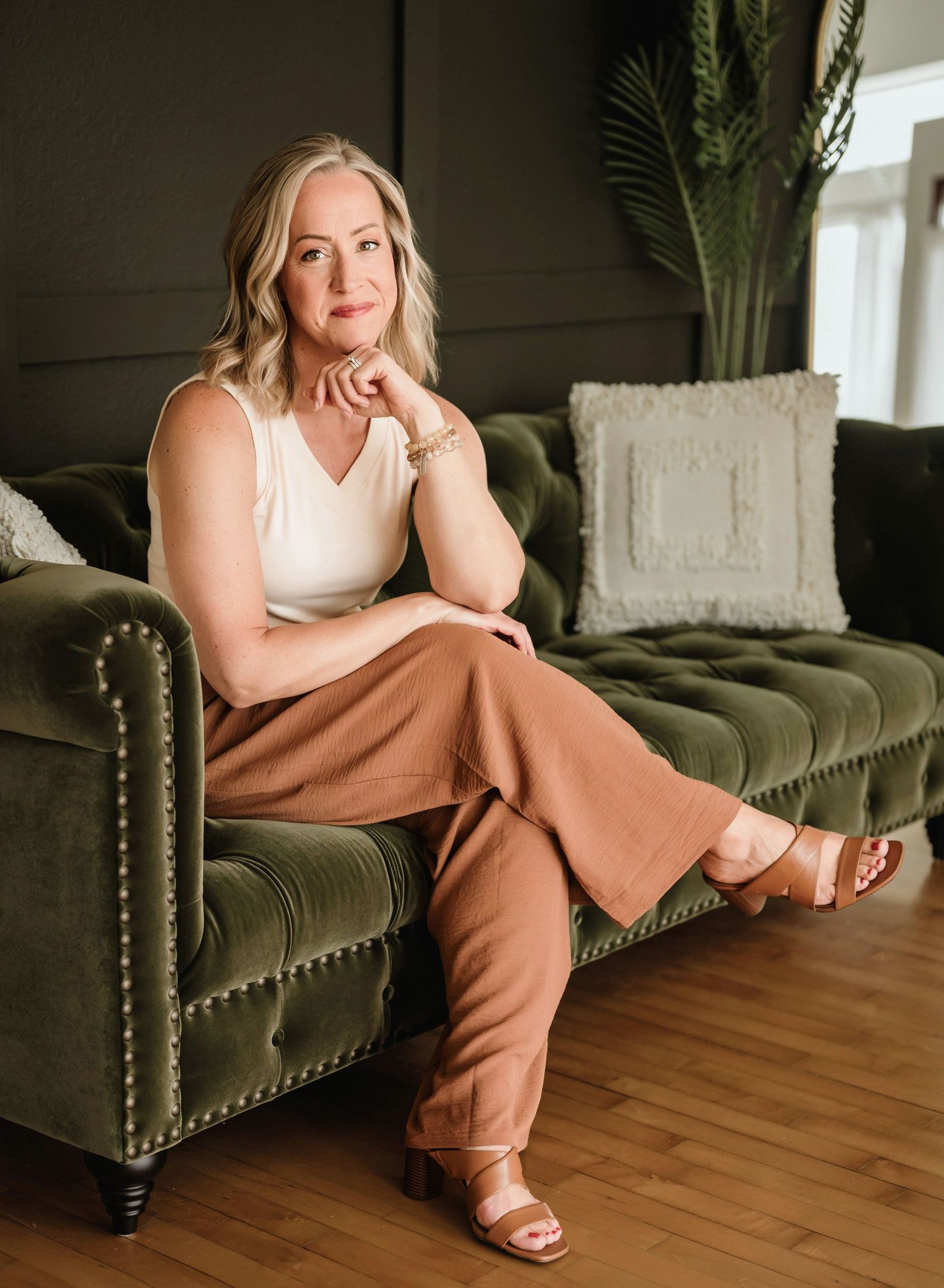 Someone sitting on a green tufted velvet sofa wearing brown pants and a white tank top in a modern living room.