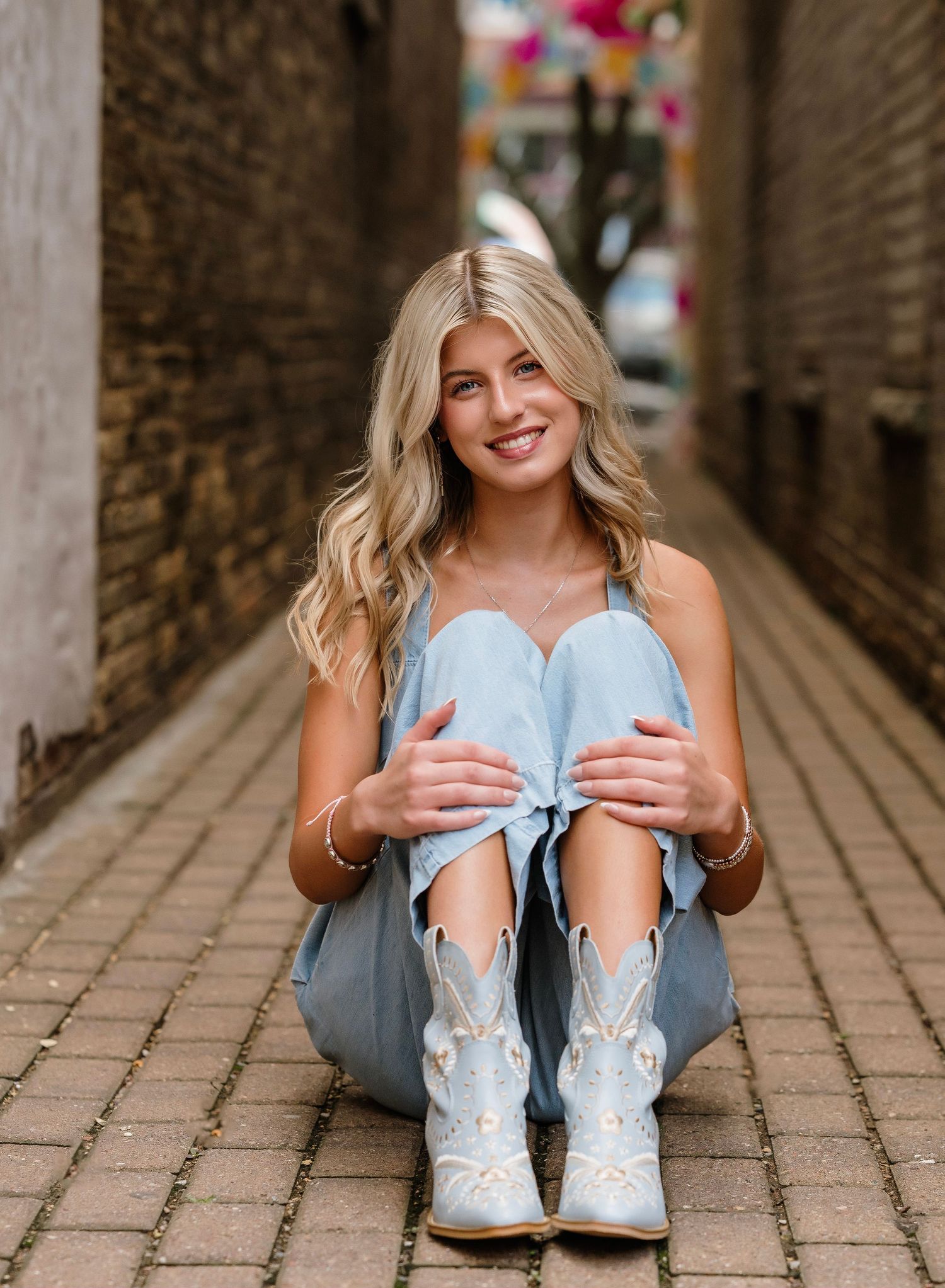 A person wearing ripped jeans sits on a rustic wooden bridge showing off decorative white cowboy boots.