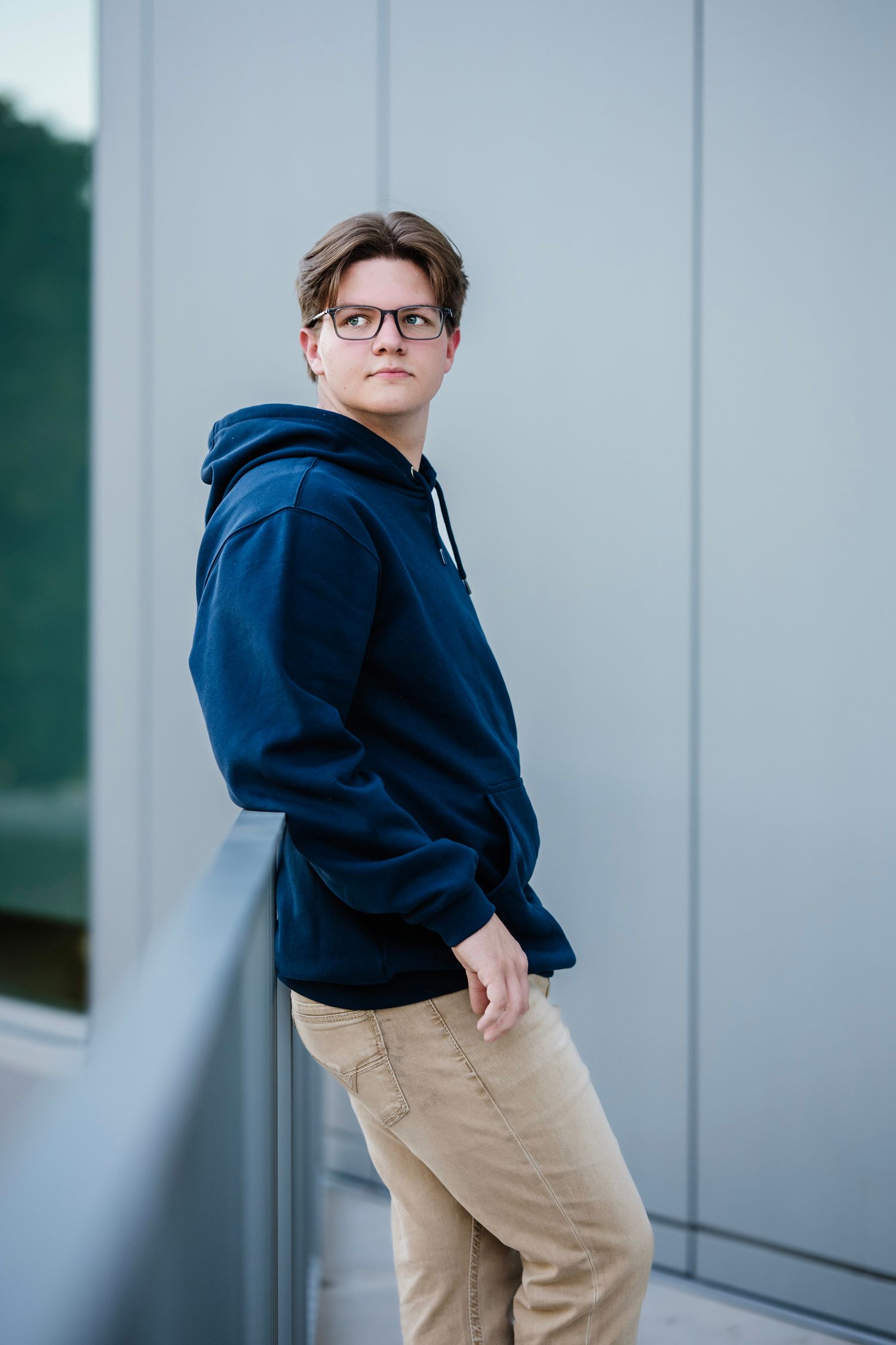 A person wearing a navy hoodie and khaki pants poses against a gray wall in four different angles.