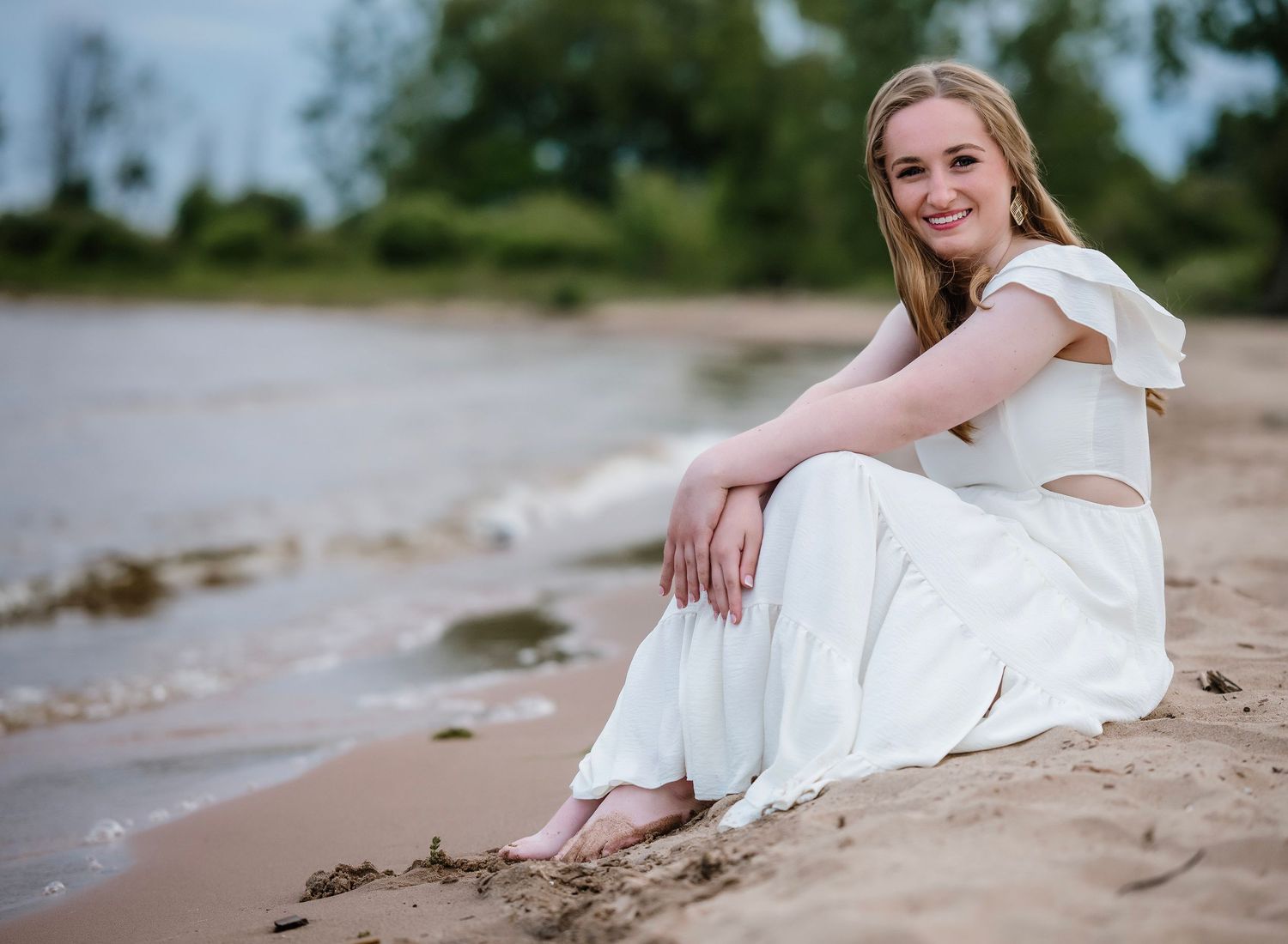 A bride in a white wedding dress reclines on a sandy beach during a coastal photoshoot.