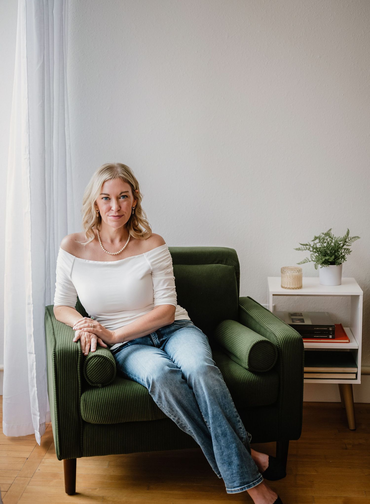 Someone relaxes on a plush green armchair in a bright room with white walls and minimal decor.