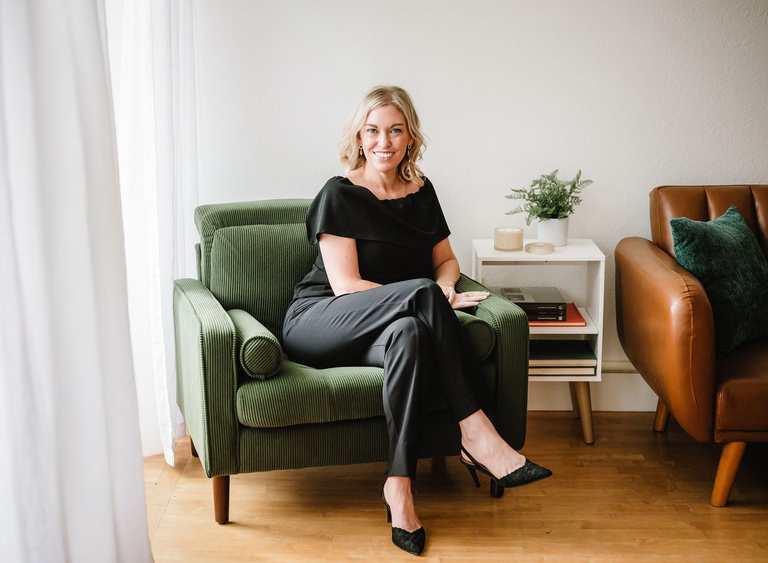 Person in black outfit sitting in multiple poses on a brown floor with green chair and white curtains in background.