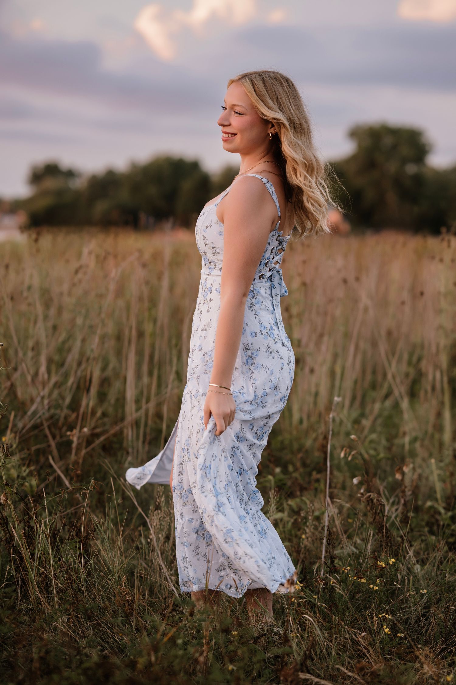 Blonde woman in a white floral sundress standing gracefully in a golden field at sunset.