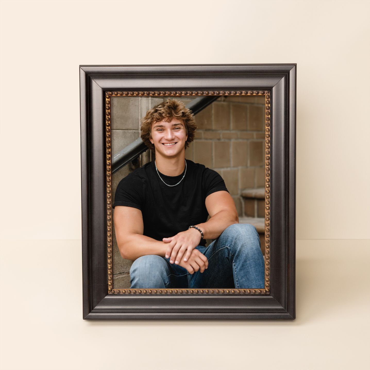 Three framed portrait photographs arranged horizontally on a light colored wall show casual poses in dark frames.
