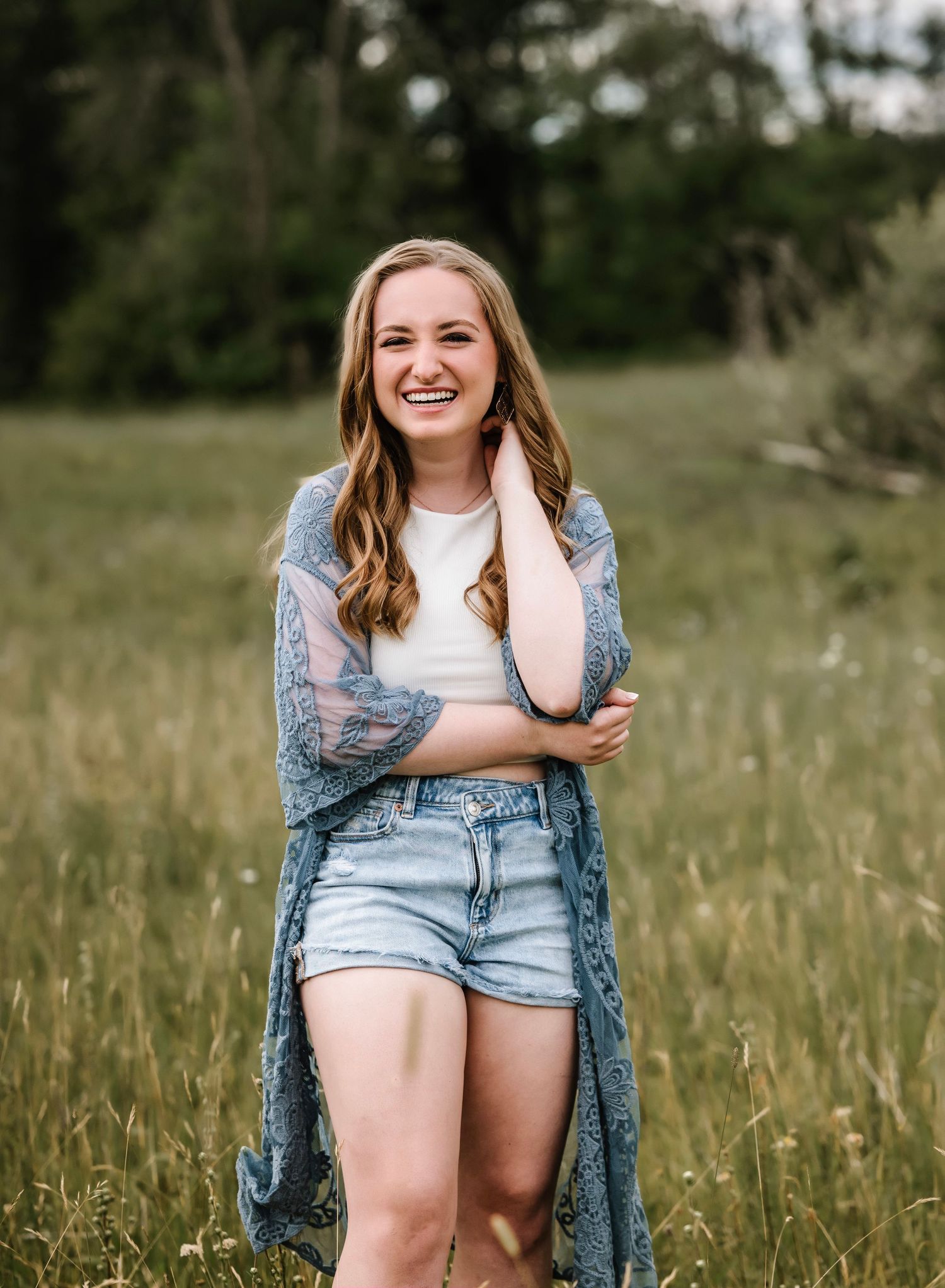 A candid photo series of someone wearing denim shorts and a blue cardigan laughing joyfully in a grassy meadow.