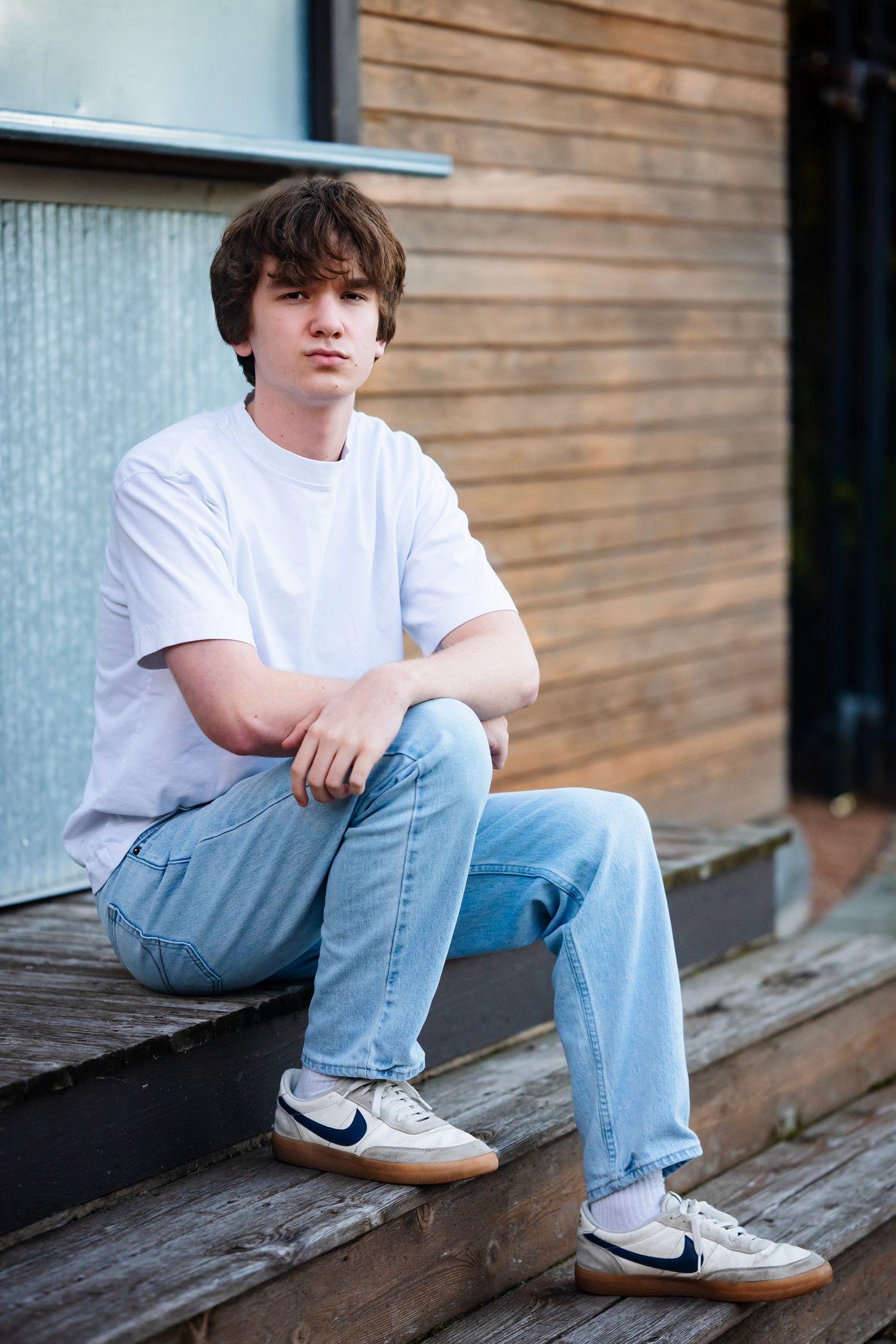 A person in a white t-shirt and light blue jeans sits casually on wooden steps wearing Nike sneakers.