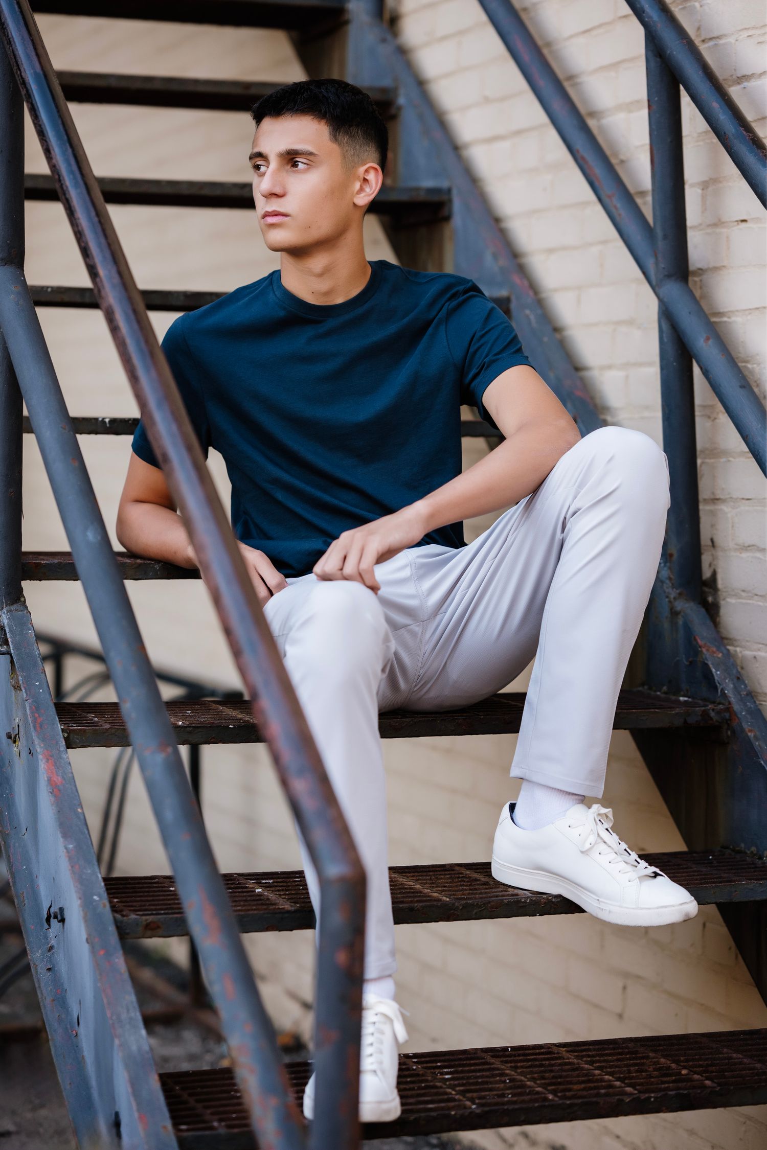 Person wearing white pants and navy shirt sits casually on modern metal stairs with clean architectural lines.
